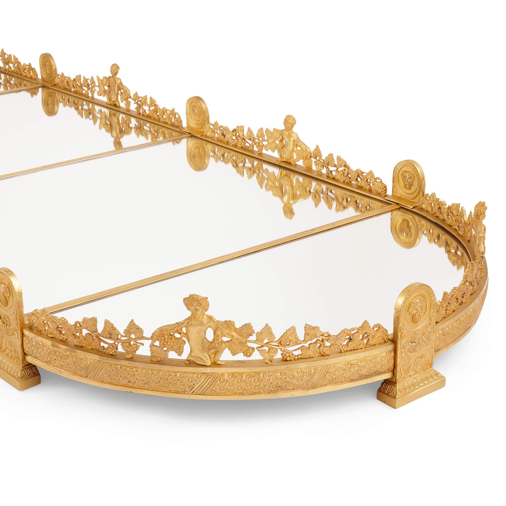 Empire style gilt bronze and mirror surtout de table centrepiece 
French, 20th Century
Height 13.5cm, width 318cm, depth 66.5cm

This French-crafted table centrepiece, or 'surtout de table,' stands as a testament to the heritage of European grand