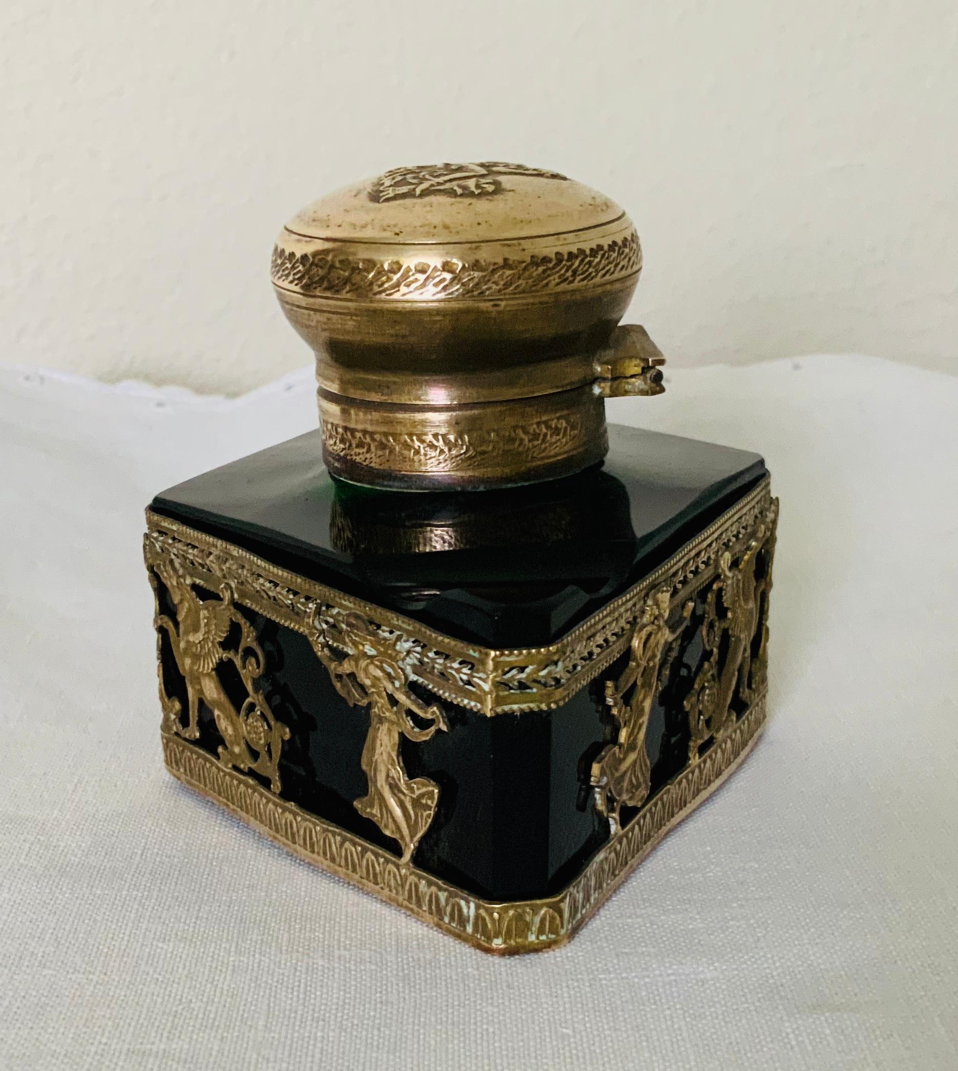 Se trata de un tintero pesado de cristal verde esmeralda en forma de paralelogramo de estilo Imperio. Está montado en bronce culpabilizado con una escena de estatuas esfinges, jarrones en forma de campana y doncellas que se mueven y sostienen