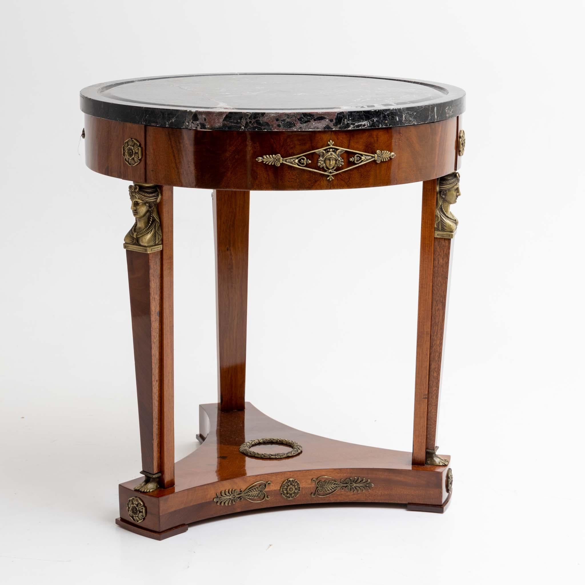 Empire style gueridon with three legs and trefoil base. The legs are decorated with caryatid-herms. The tabletop is made of a dark gray marble with red veins and the smooth frame as well as the pedestal are adorned with other Empire style fittings.