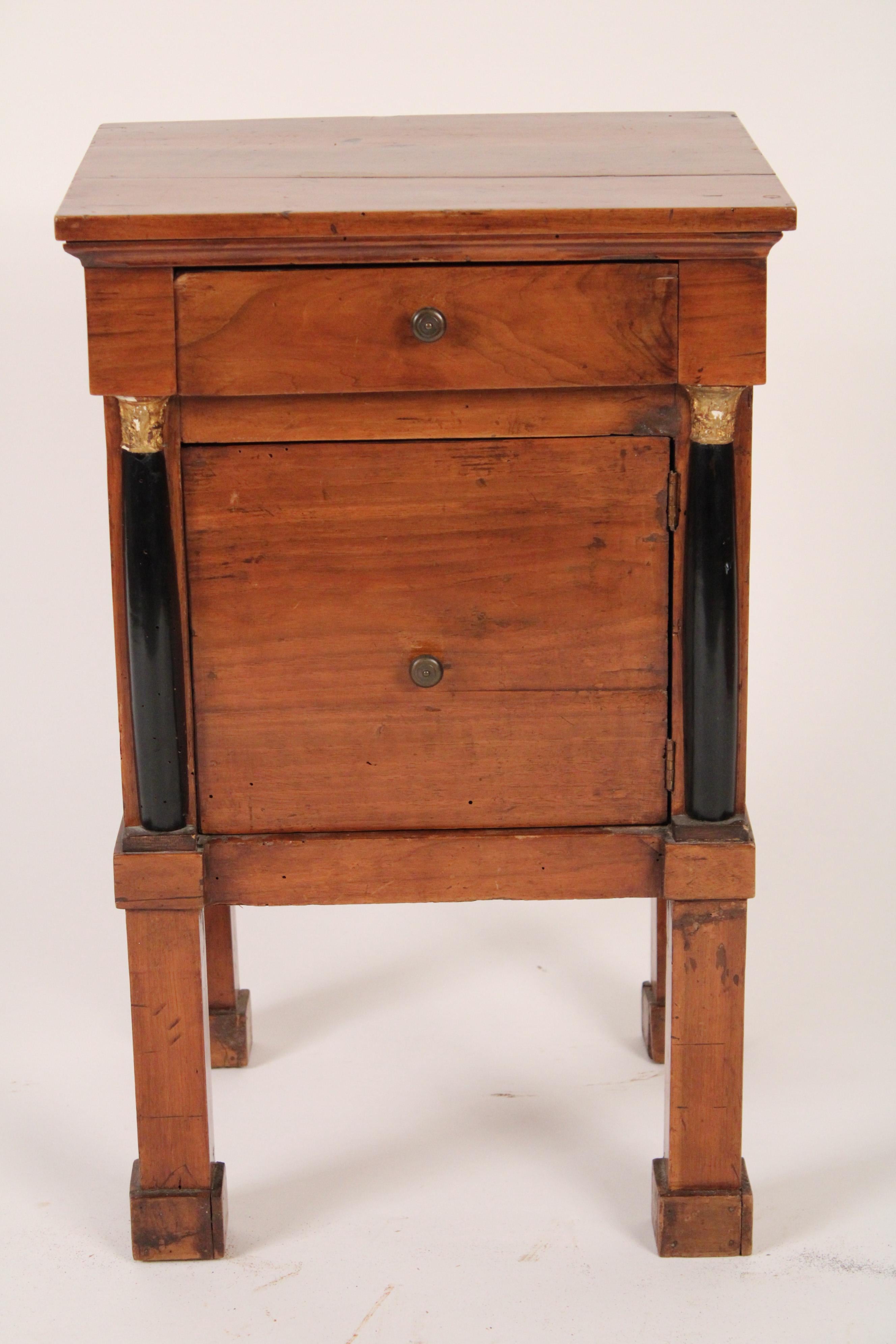 Italian Empire style fruit wood comodini, circa 1900. With a square top, a drawer and a door, black lacquered columns with gilt capitals on square legs and feet.