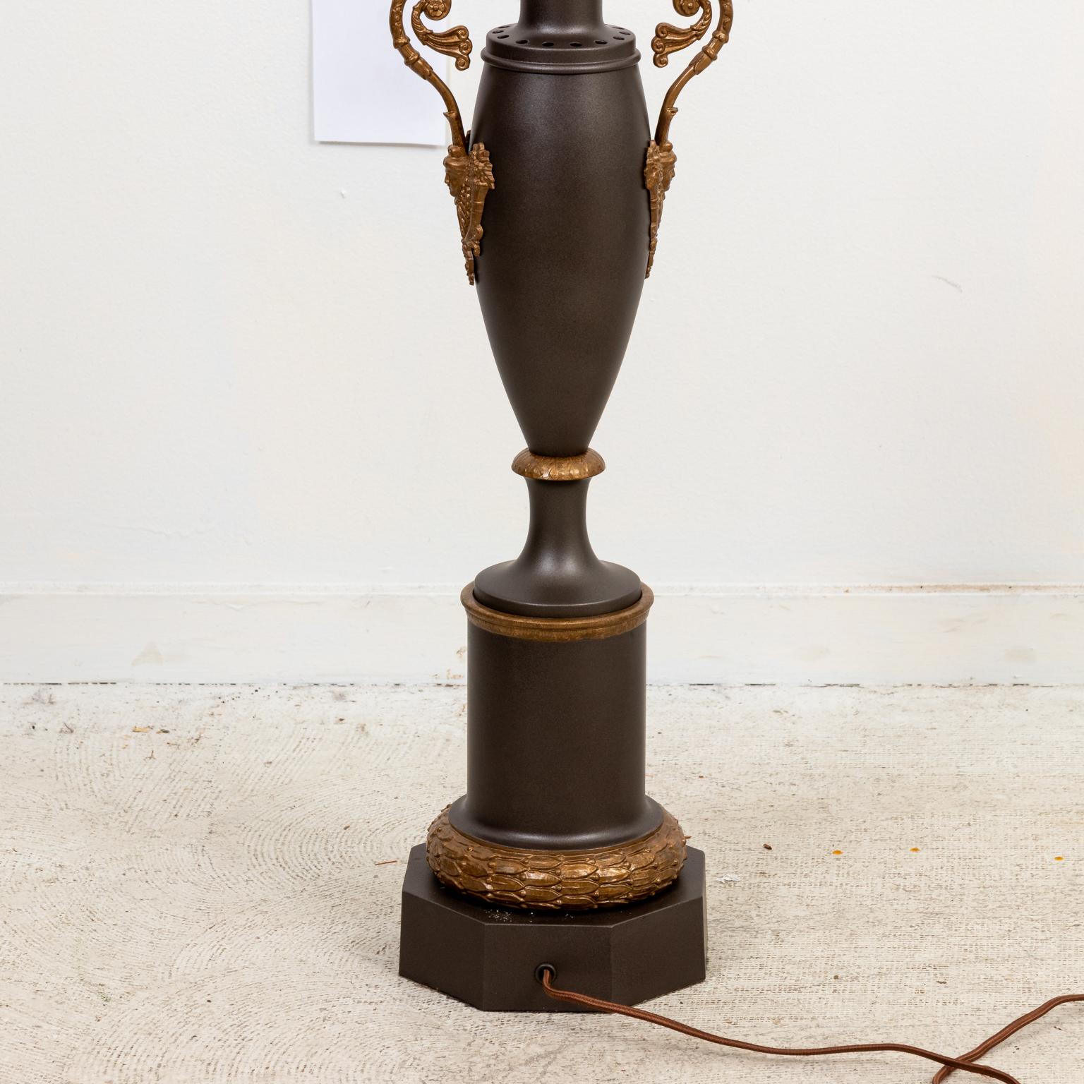 Circa 1990s Empire style metal urn shaped lamp in a gunmetal finish with scrolled arms and motifs of Cornucopia on the sides. Please note of wear consistent with age. Shades not included.