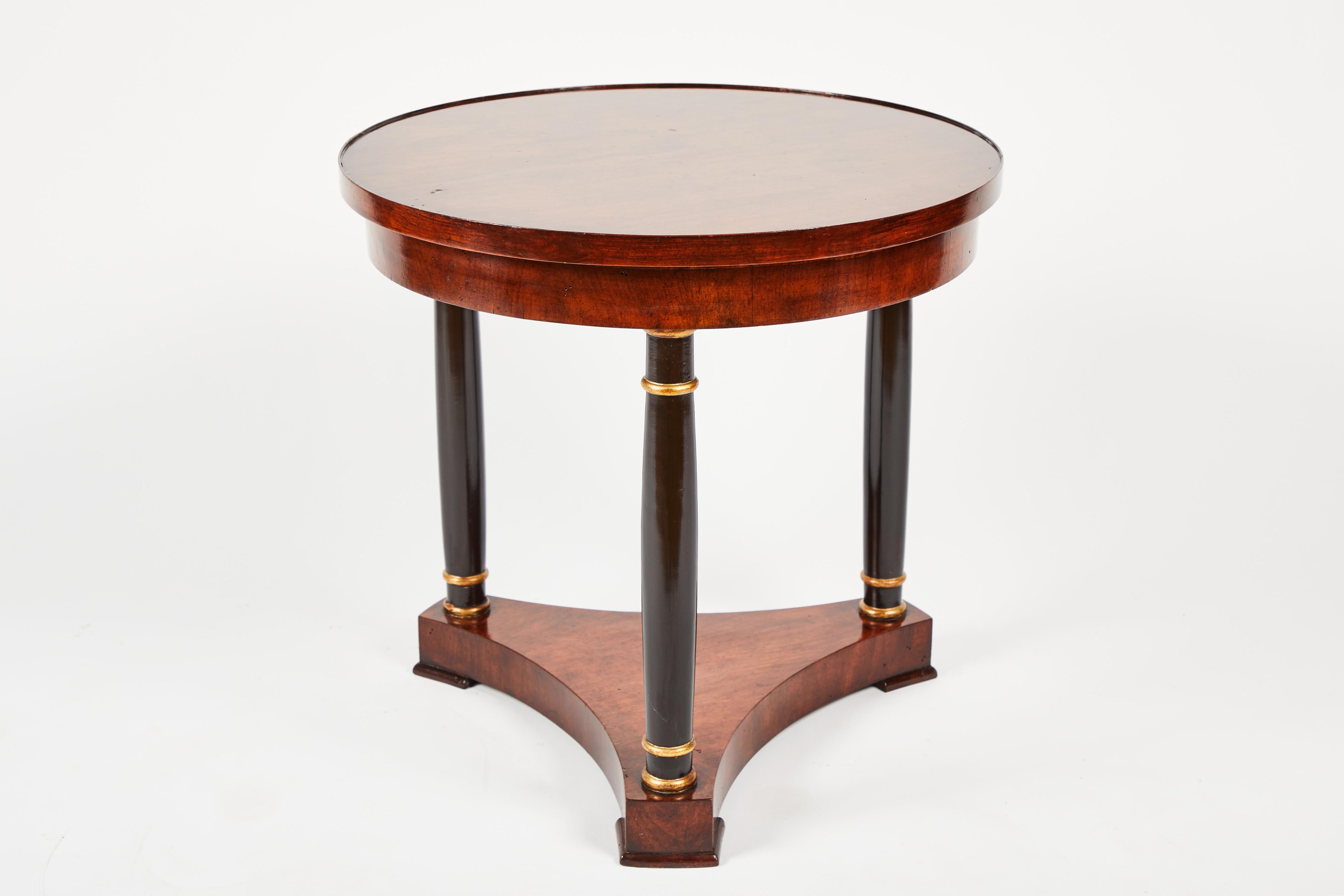 Beautiful and restored Empire-style Mahogany side table. Round Mahogany top and base with new polish, three ebonized legs with dual ring gilt-wood accent details. In great, restored condition.