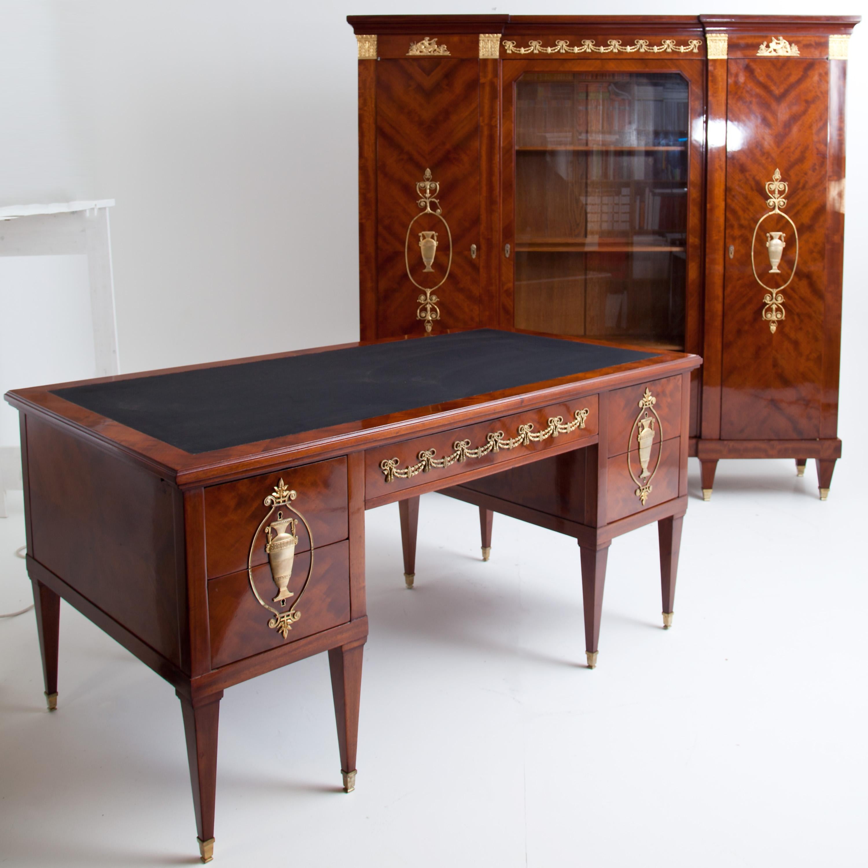 Large Empire style, mahogany veneered desk. The desk stands on tall square legs with brass sabots and features gilded Empire style appliqués in the form of urns, arabesques and festoons. The table top can be pulled out on both sides and is covered