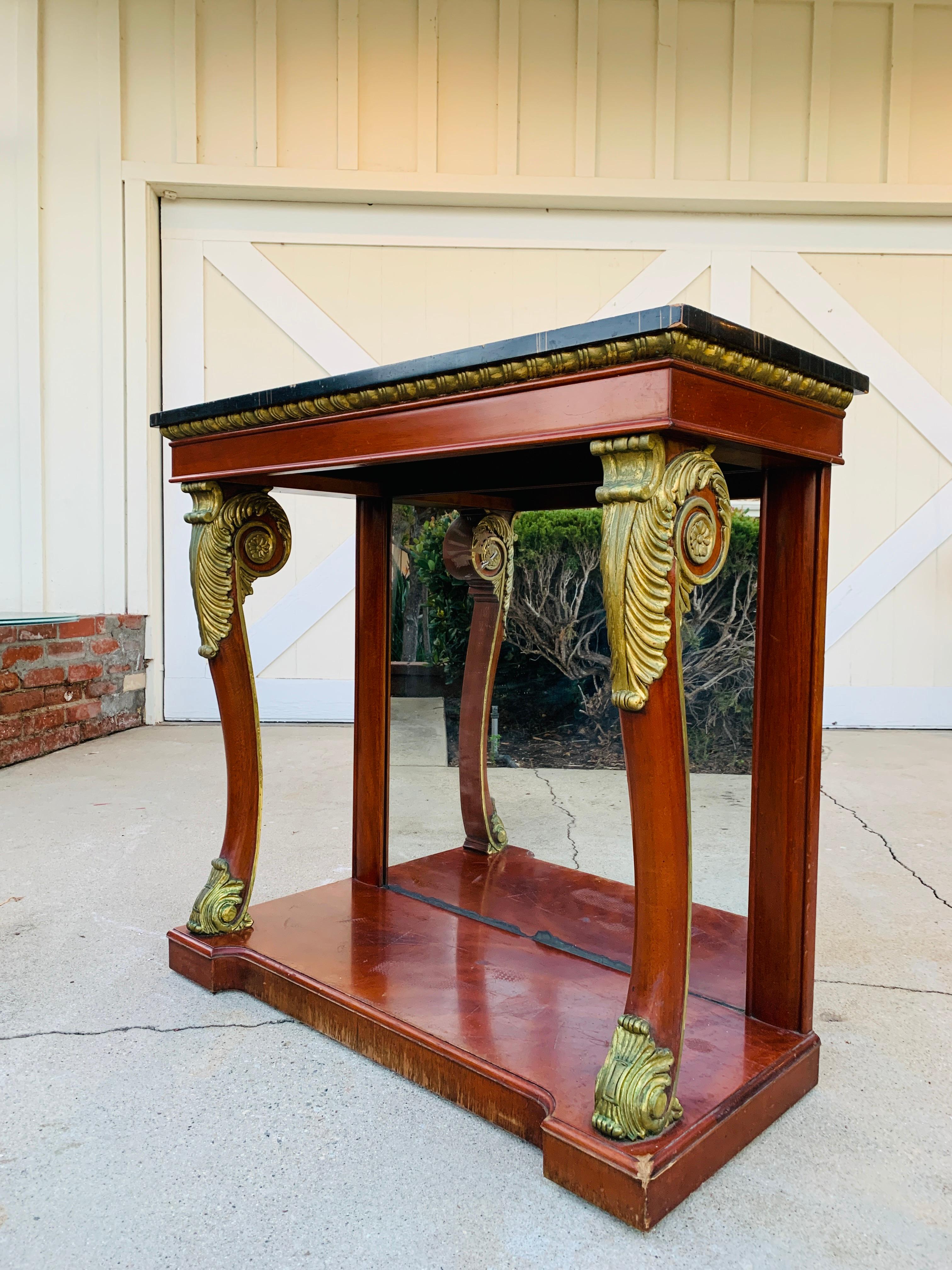 French Empire style console or entry table made in mahogany wood having gold gilt wood carvings.

The table has a faux marble top and am mirrored back. The table was made by Kindel Furniture retaining the original label and finish.

The back of
