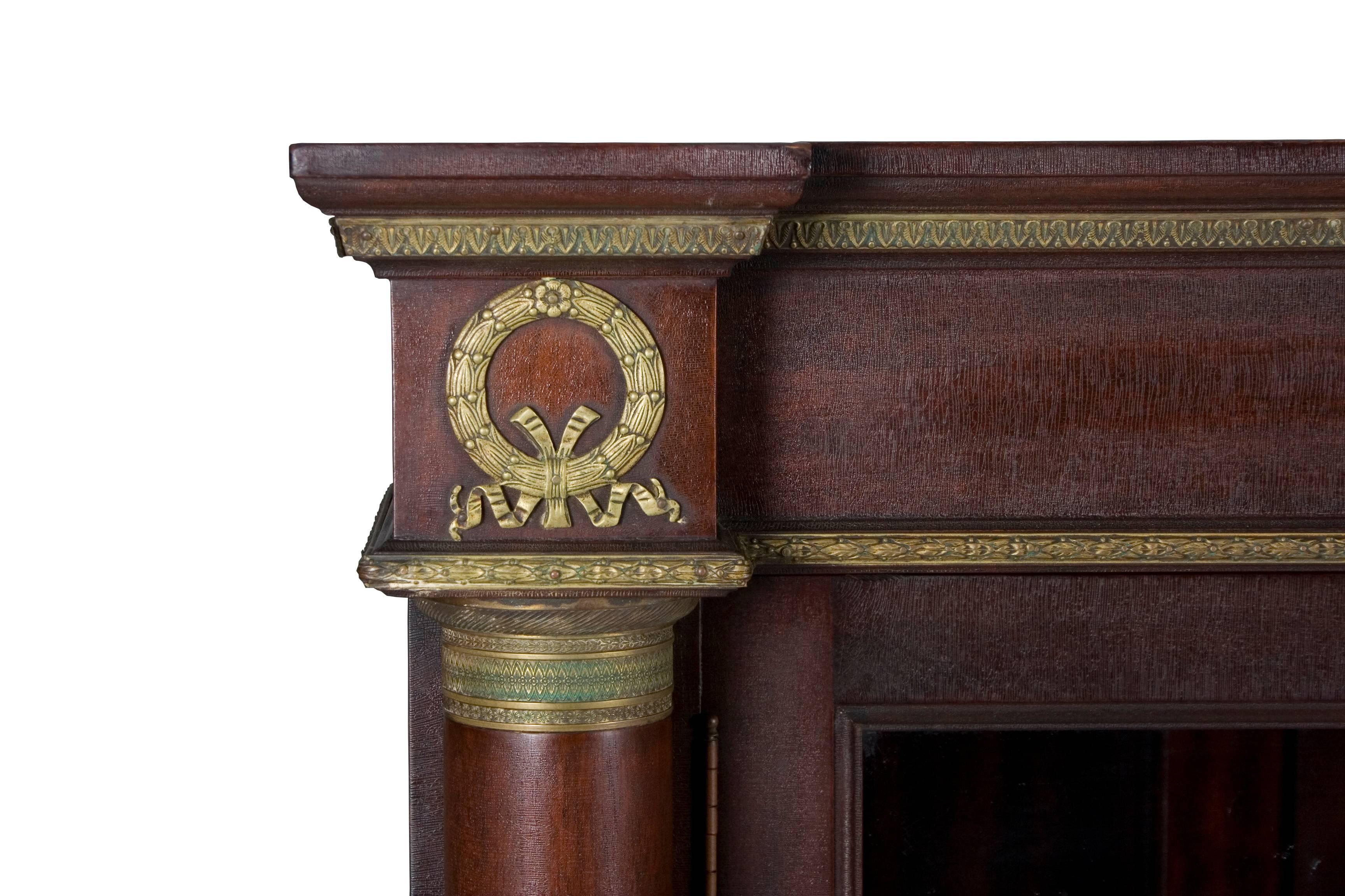 This bookcase is a stunning piece done in the Empire style. Recently imported from Europe, we estimate it was made circa 1960. It features a dark mahogany wood with brass ormolu decorations and large paw feet on casters. Two smooth columns flank a