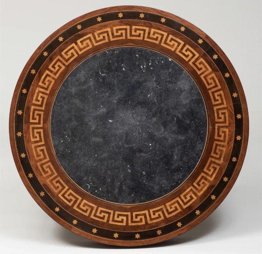 The circular table with contrasting marquetry of star decoration on the outer rim and then stylized greek key below it
with a black fossilized marble top with white highlights. Slight seam separations, slight warping to the top,age splits alonge