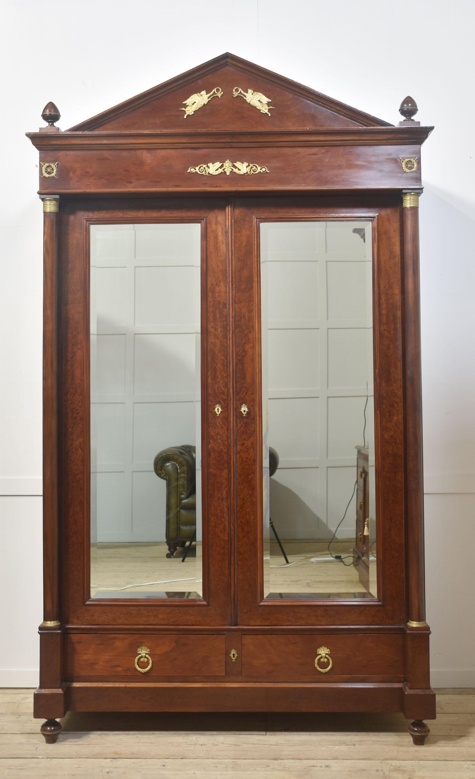 Empire-Garderobe mit abnehmbarem Gesims mit Messingdekor, flankiert von gedrechselten Endstücken. Darüber befinden sich zwei große, abgeschrägte Spiegeltüren, die sich öffnen lassen und einen großen Hängebereich freigeben. Flankiert von Rundsäulen