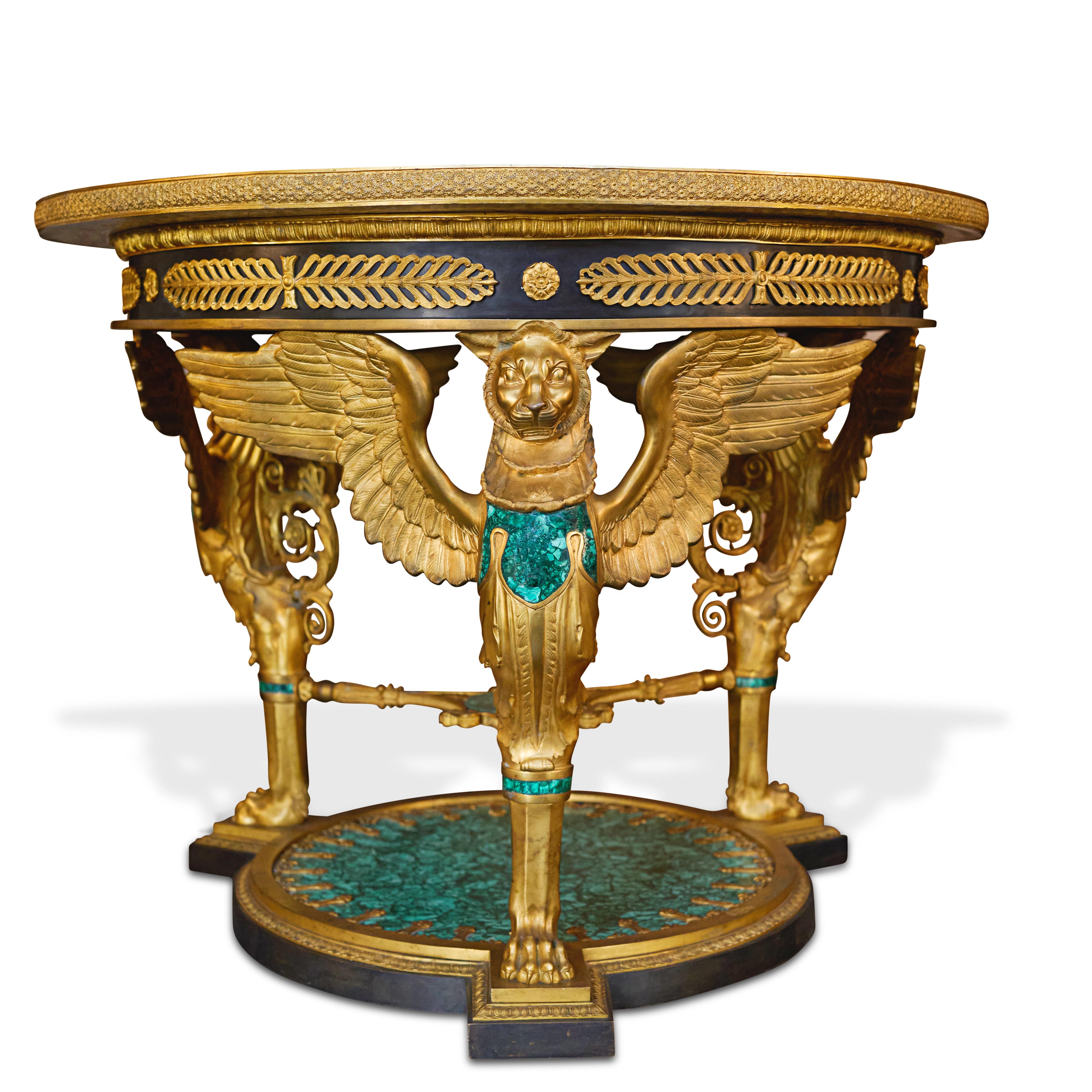 Une grande et impressionnante table centrale de style Empire en bronze doré et malachite. La table présente un plateau circulaire magnifiquement incrusté de malachite et bordé de bronze doré, surmontant une frise où alternent rosettes et anthemia,