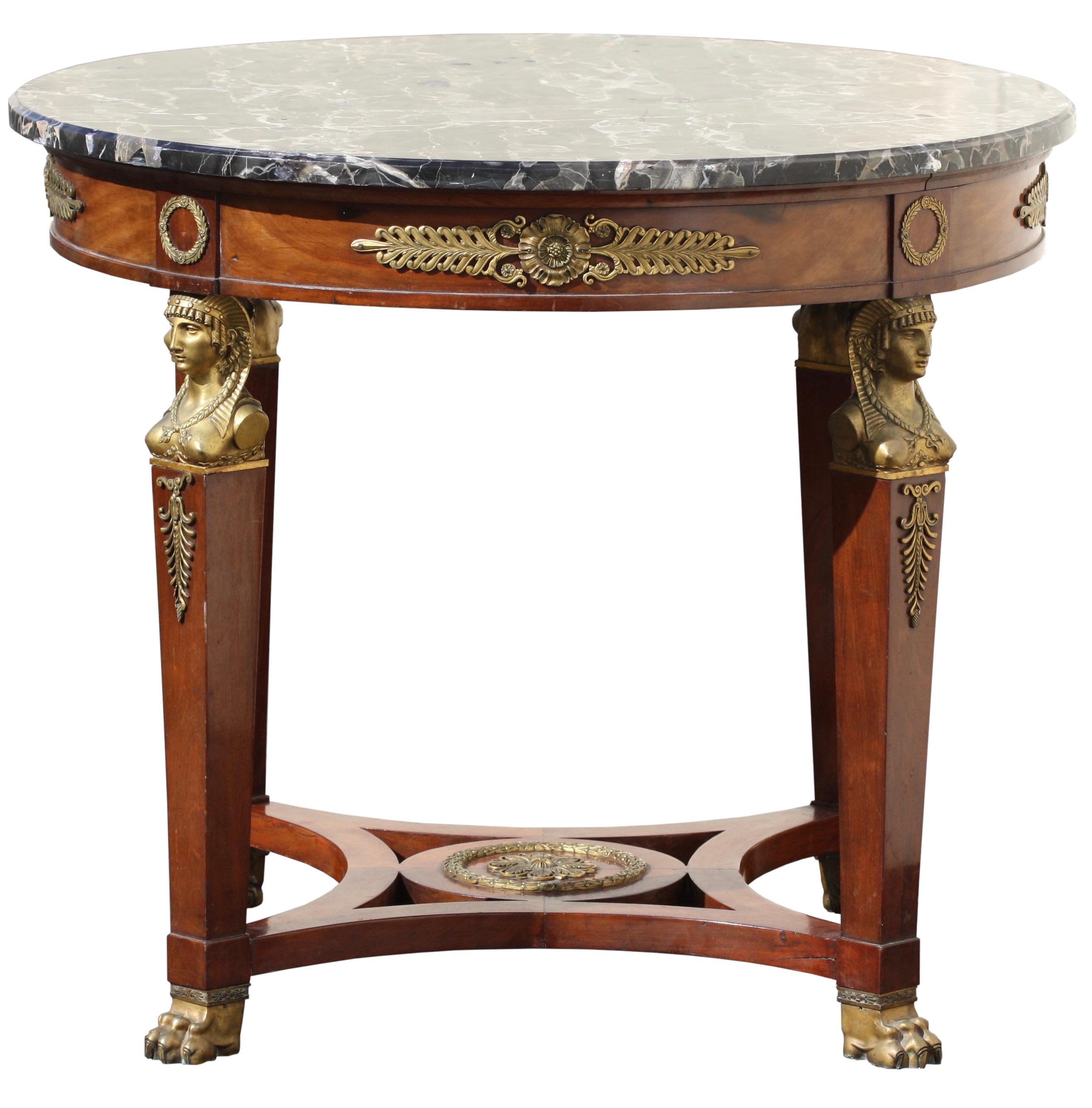 An Empire style ormolu-mounted mahogany marble top center table, late 19th century.
The circular portoro marble top above a frieze applied with anthemia, rosettes and laurel wreaths, raised square tapered legs each headed by a female Egyptian bust,