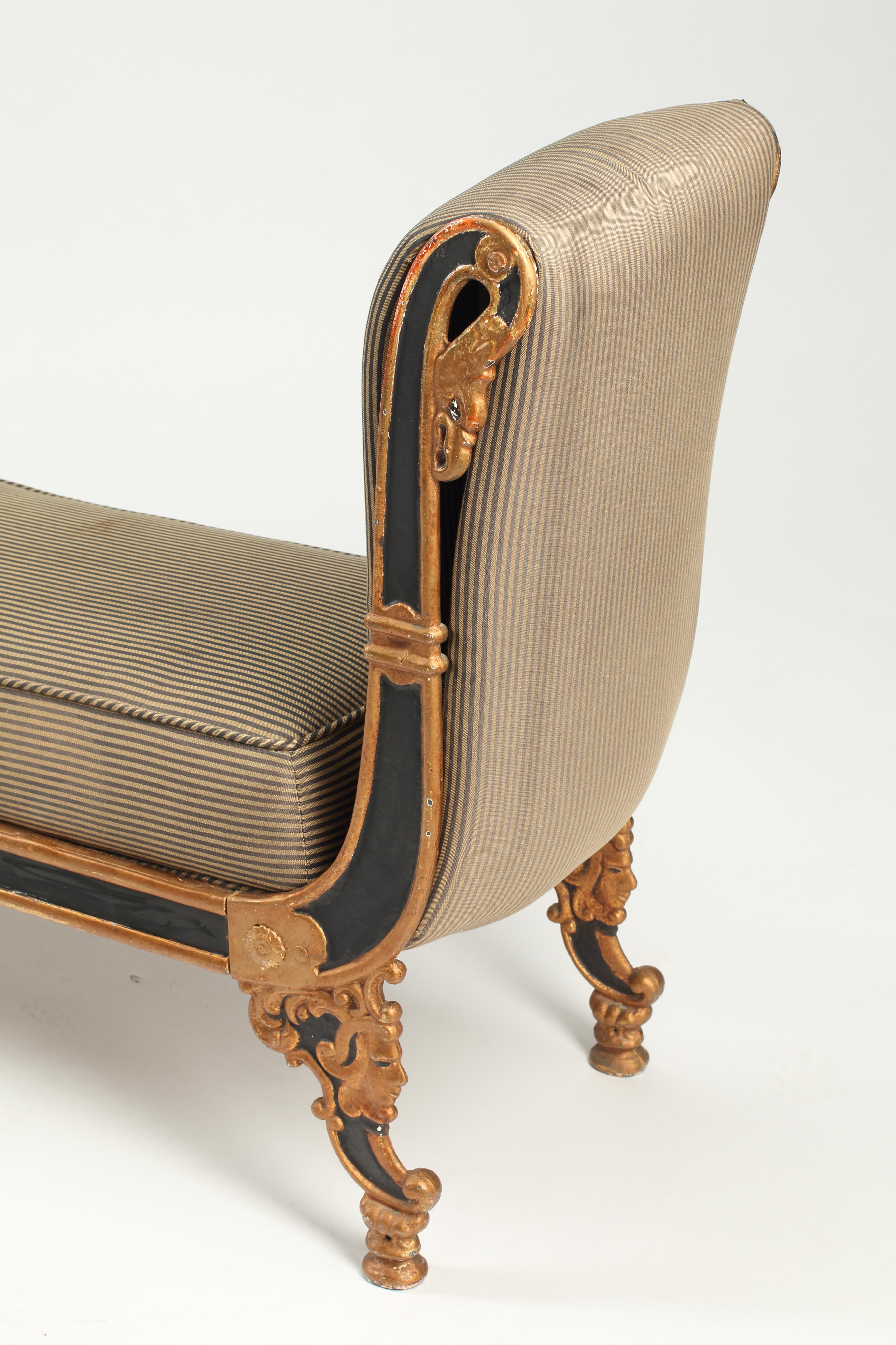A highly decorative and unique 19th century French empire painted and parcel gilt cast iron upholstered bench.
Parcel gilt border is of a rich gold with warm red undertone painting jester faces, curves and rosettes. 
Upholstered with elegant and