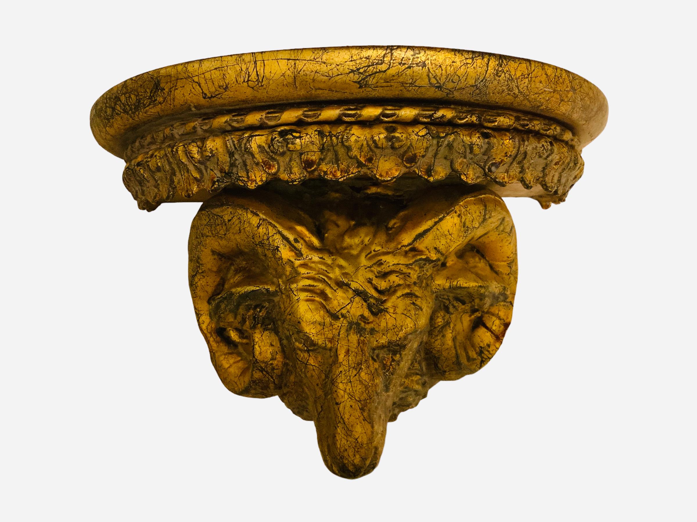 This is a pair of gilt wood ram’s head wall brackets/shelves. They depict a half moon shaped top shelves. They are decorated with a carved garland of acanthus leaves below the top. Their bodies are shaped as large ram’s heads with scrolled horns.