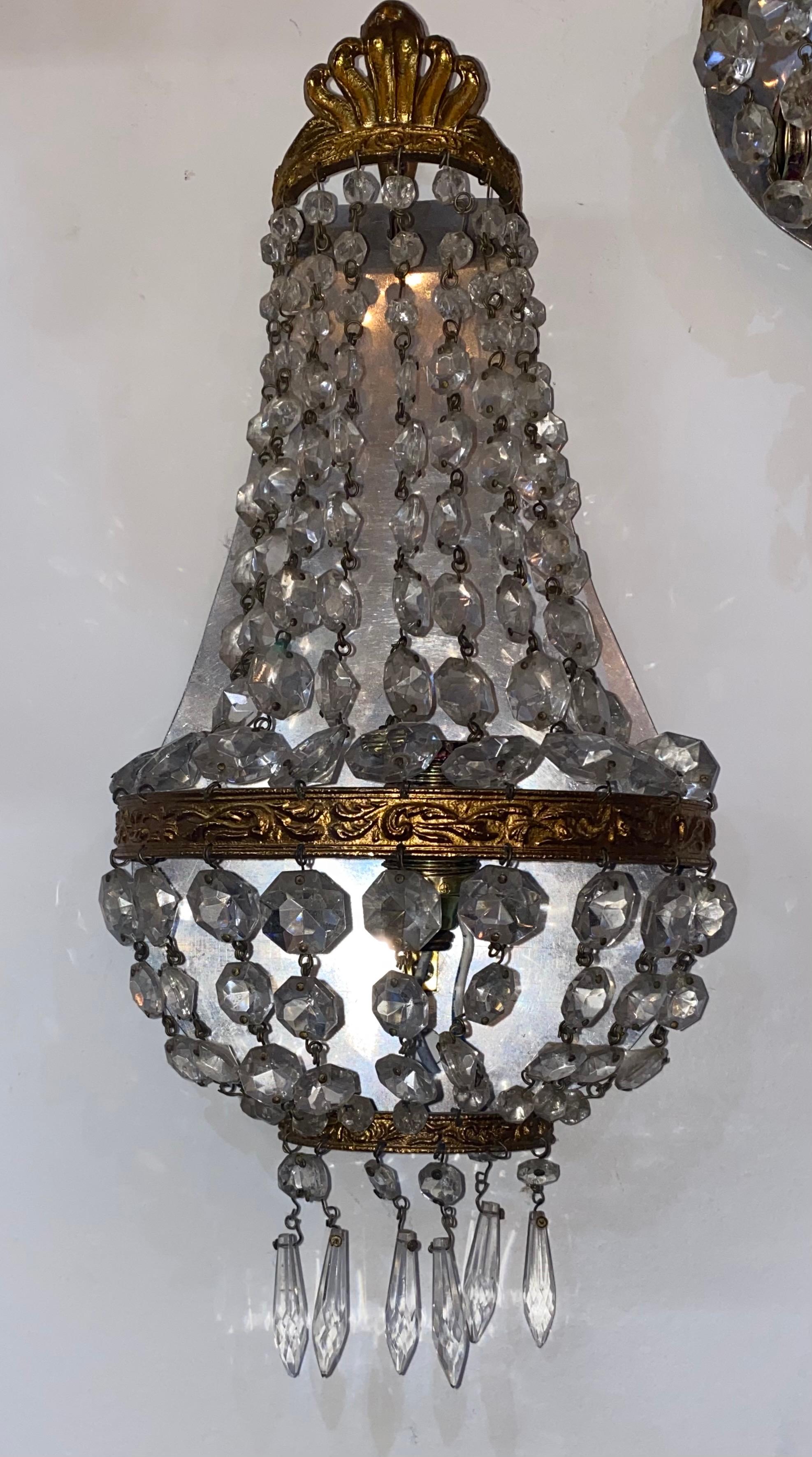 Empire style crystal prism wall sconces, 20th c., having reflective white metal wall plate, fitted with gilt metal mounts, hung with strands of hexagonal prisms, concealing one light fixture, American wired and certified.