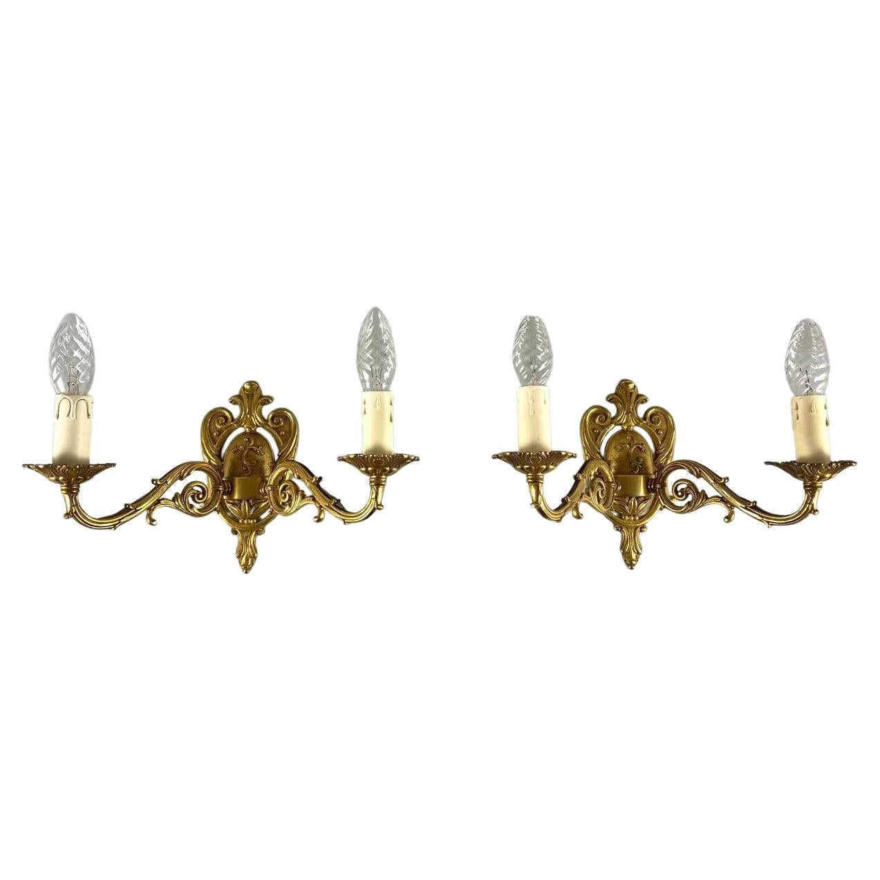 Paired vintage wall sconces in gilt brass, artistic casting.

Floral motif with classic swirl.

Each sconce consists of a base and two curved arms emanating from it, skillfully finished with chasing by hand.

The horns of the sconces are