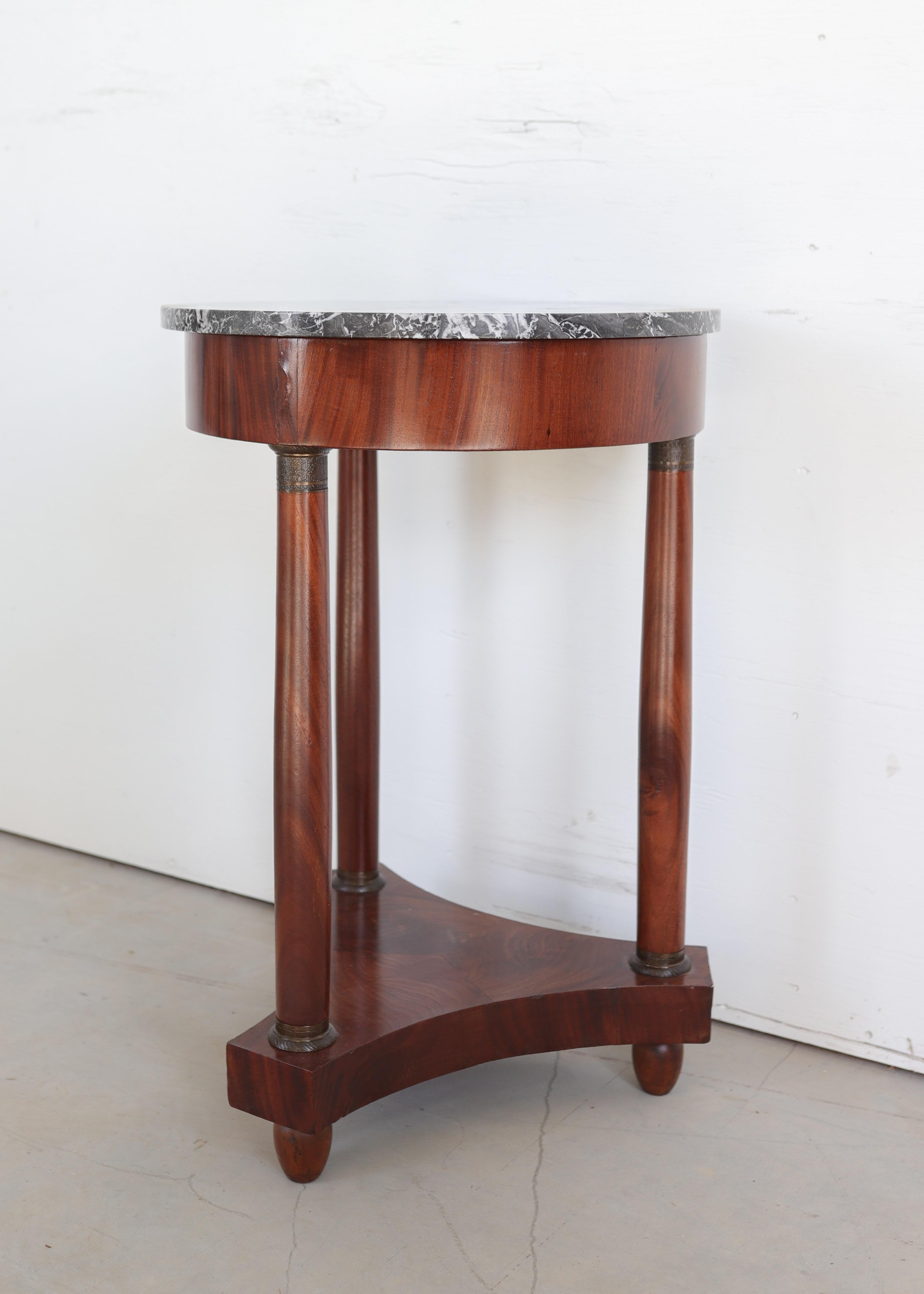 Ce guéridon raffiné de style Empire du XIXe siècle, fabriqué en placage de noyer, présente un majestueux plateau circulaire en marbre gris reposant sur une base colonnaire néoclassique. La table est soutenue par quatre élégantes colonnes ornées de