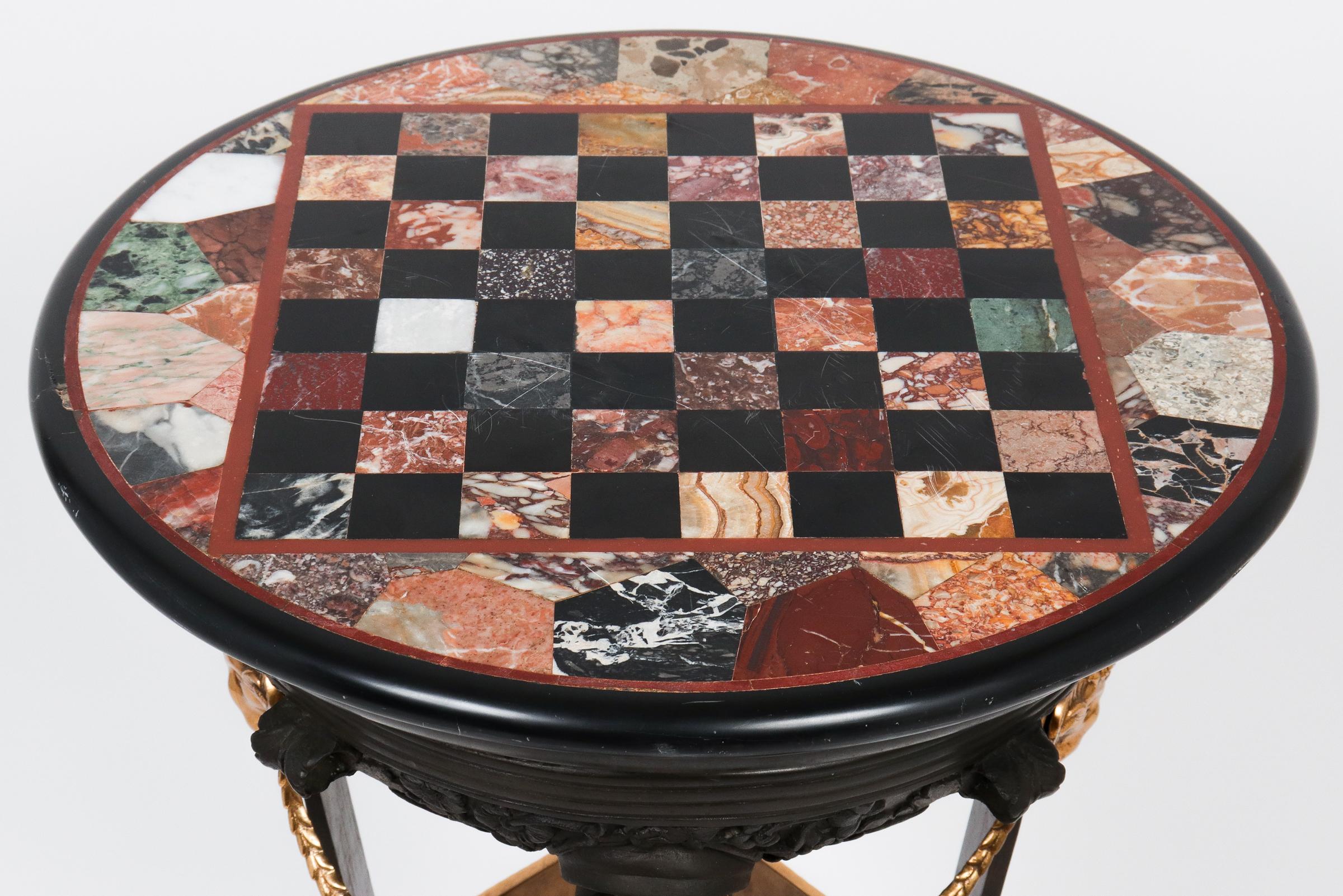 Empire style Grand Tour bronze gueridon or pedestal table with a circular pietra dura marble games top, gilt bronze rams head, paw feet, and swag details, mounted on square platform base. In great antique condition with age-appropriate wear and