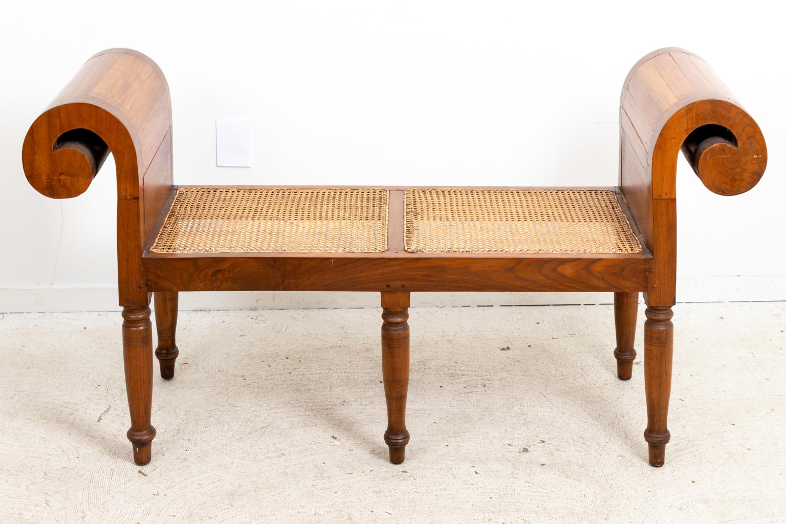 Empire style scrolled arm bench with cane woven seats. The bench is supported by six turned legs on arrow feet. Please note of wear consistent with age including patina, chips, and minor scratches to the wood. The cane also has minor finish loss.