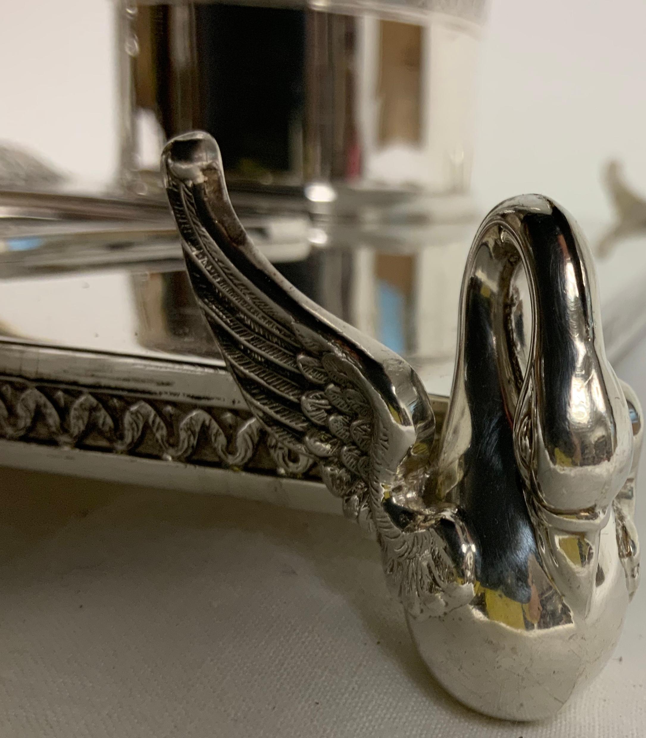 This is a unique polished silver double inkwell tray. It is composed of two wide cilynder shaped inkwells decorated with an embossing of a garland of palmettos in the upper border. The neck of two swans are joined together over their lids and above