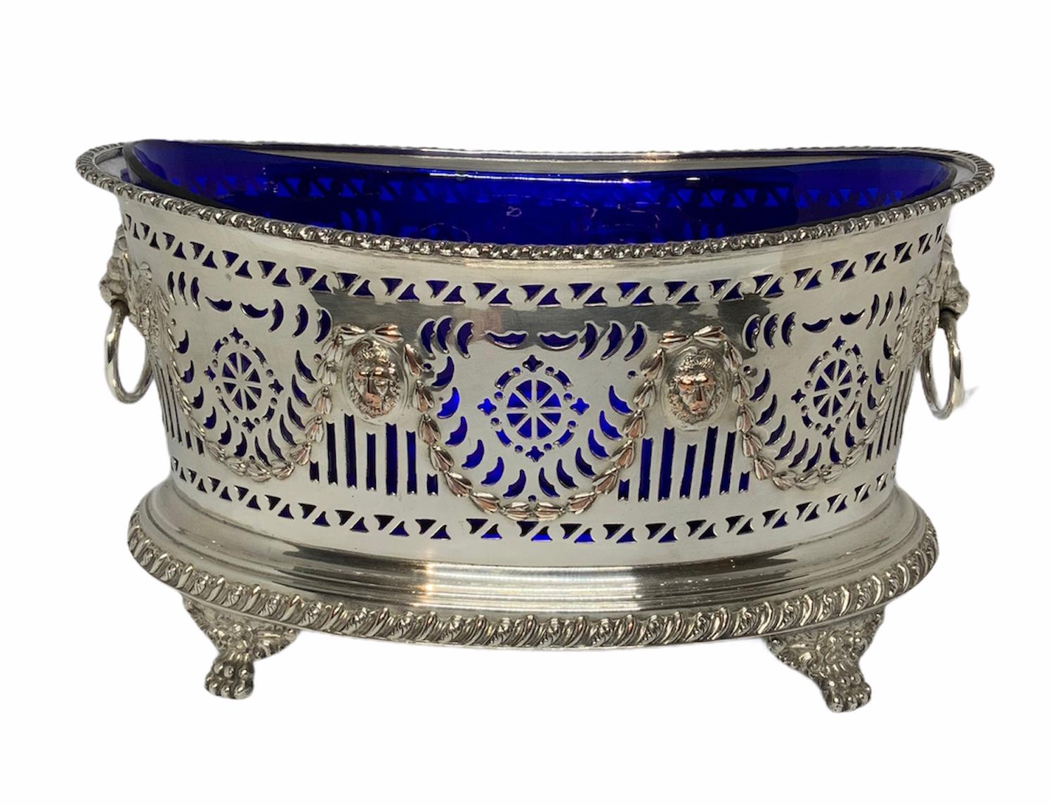 This an Empire style silver plate cobalt blue glass oval bowl centerpiece. The reticulated bowl is decorated with a garland of laurel leaves alternated by a repousse mask of lions. The upper and lower borders of the bowl are highlighted by the