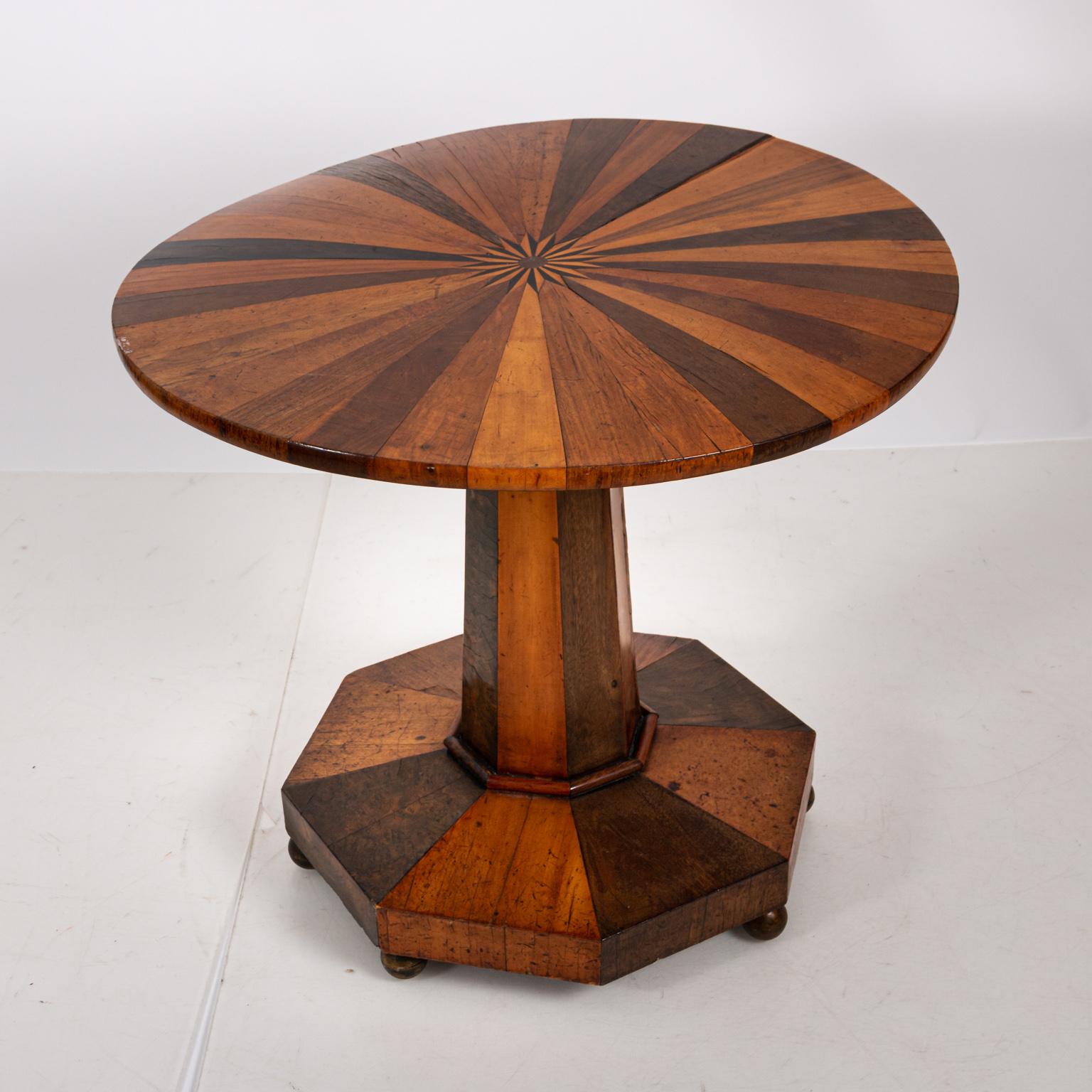 Empire style round table with over twenty-five various specimens of inlaid wood in a starburst pattern, circa 1825. Please note of wear consistent with age including chips, scuffs, and minor finish loss. There is also slight warp to the tabletop.