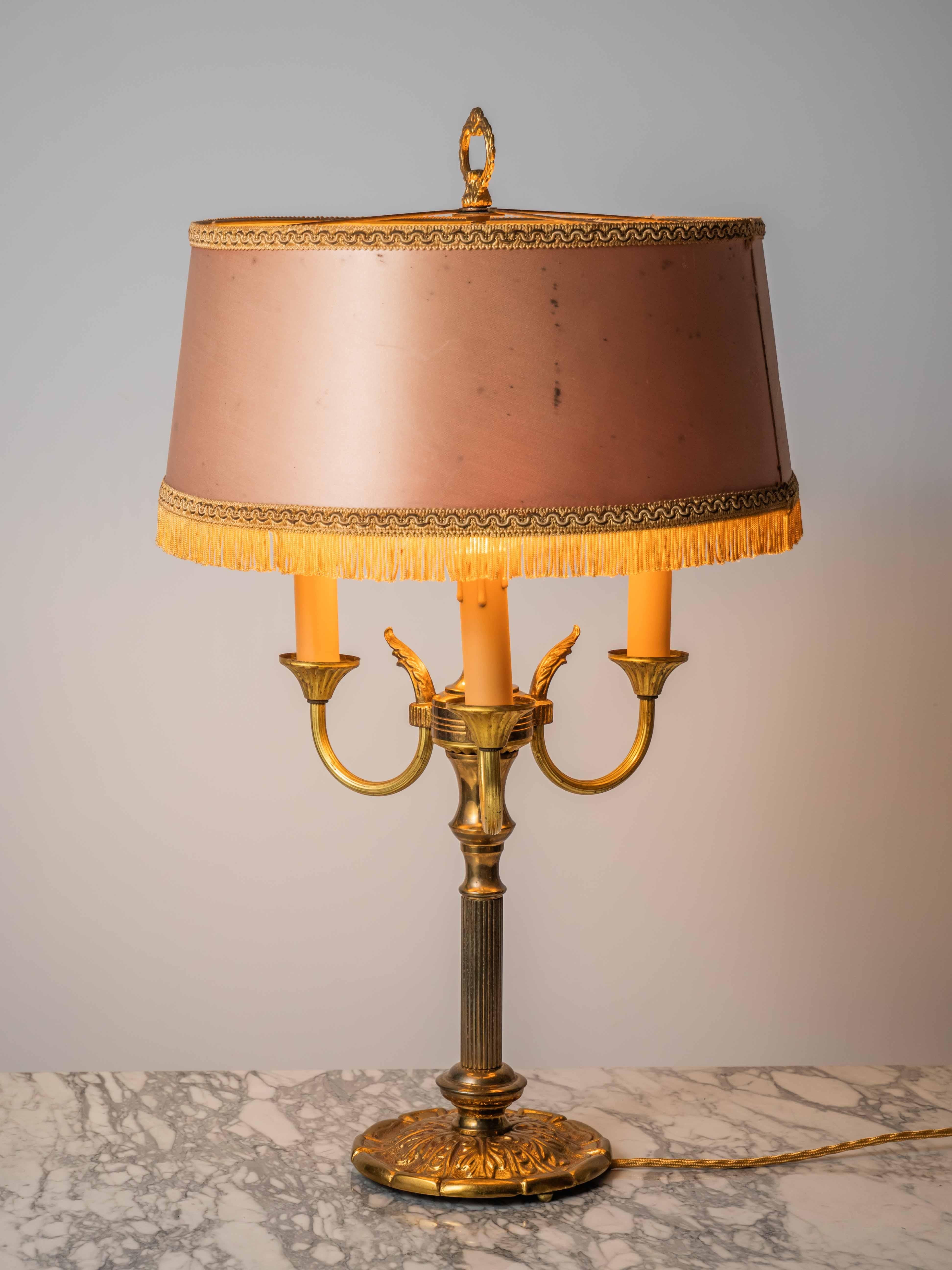 A beautiful Empire style lamp with three arms carrying bulbs. Fabric lampshade finished with a decorative port and in the lower part a decorative port with fringes. The lamp is made of brass. The lamp is for three classic candle bulbs with an E14