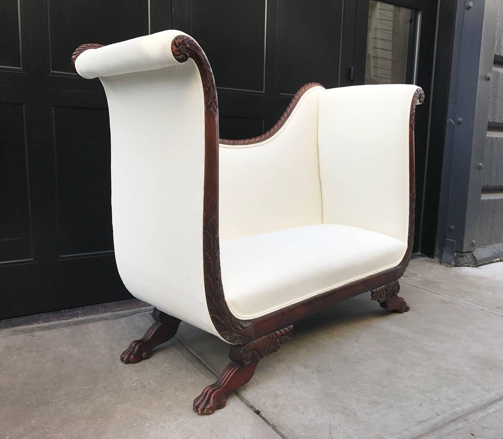 Empire style tall back loveseat with carved mahogany base and claw feet. Newly upholstered in off-white fabric.