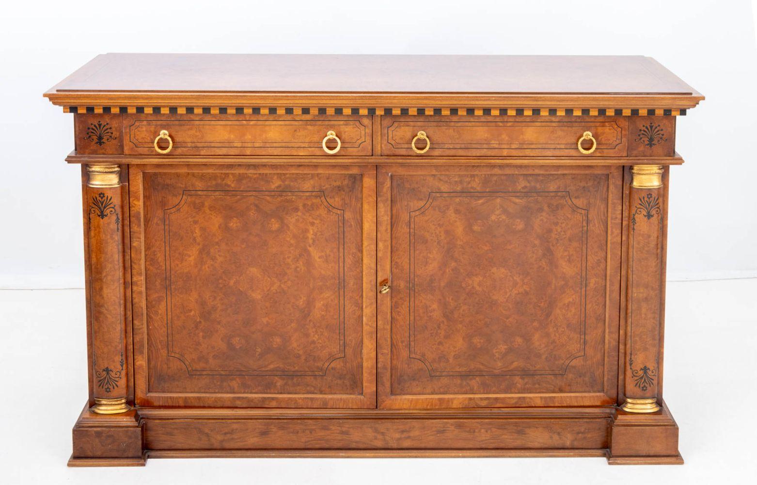 Buffet in noce stile Impero, il piano rettangolare su due cassetti a fregio con quattro maniglie ad anello in ottone sopra un mobile a due ante con quattro ripiani interni affiancati da colonne con finiture dorate e decorazioni floreali ebanizzate.