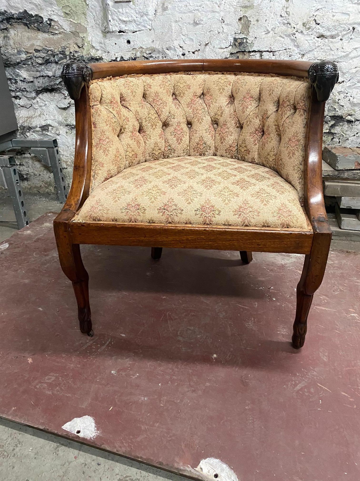 Chaise bergère en noyer de style Empire à la manière de Jacob Desmelter, avec une tête de bélier joliment sculptée reposant sur des pieds articulés.  les pieds des sabots.