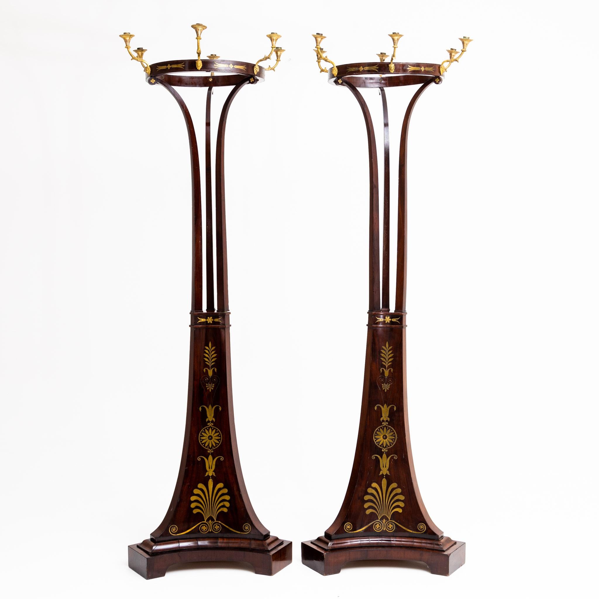 Pair of large Empire torches or candelabra on a three-pass base tapering to the top and inlaid with brass inlays in the form of acanthus leaves and floral motifs. Rising above three slender struts is the slender hoop with six fire-gilded grommets