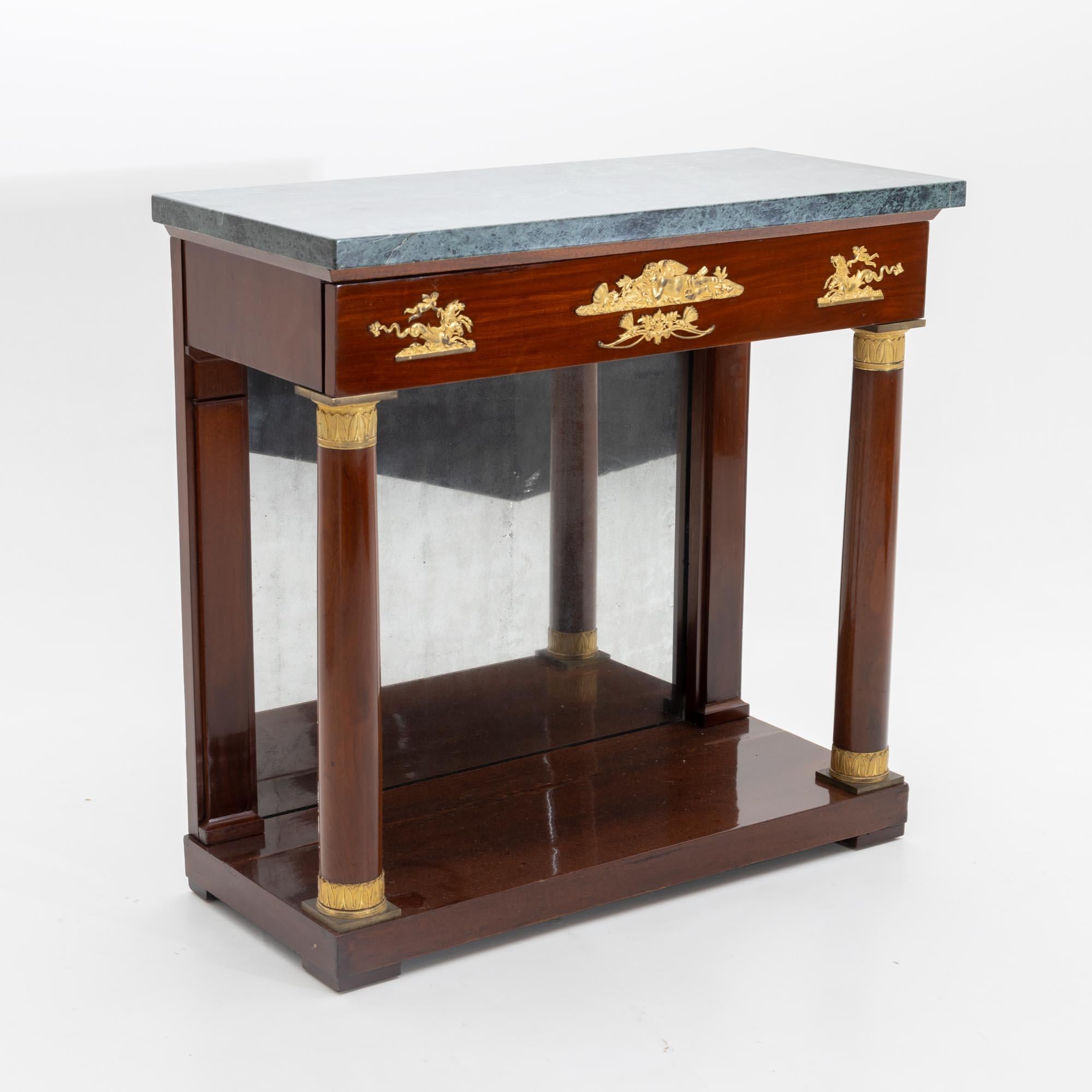Empire wall console in mahogany veneer, with one drawer and dark green marble top. The console stands on a rectangular base with two flanking columns with gold-patinated capitals and bases. The back is mirrored and the front of the drawer is