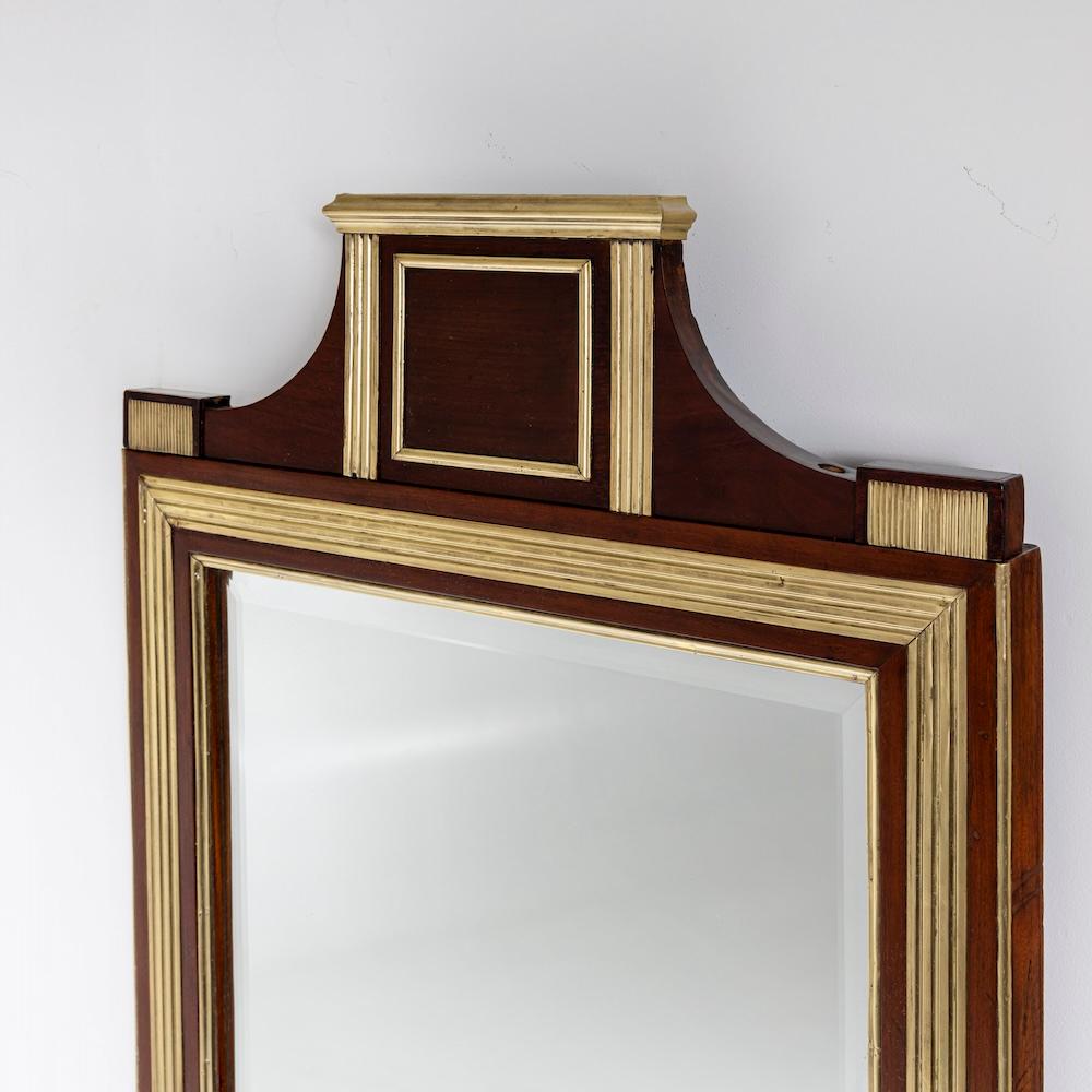 Grand miroir mural avec profils en laiton et cadre en placage d'acajou ainsi qu'un pignon s'élevant au milieu. Le verre du miroir est facetté.