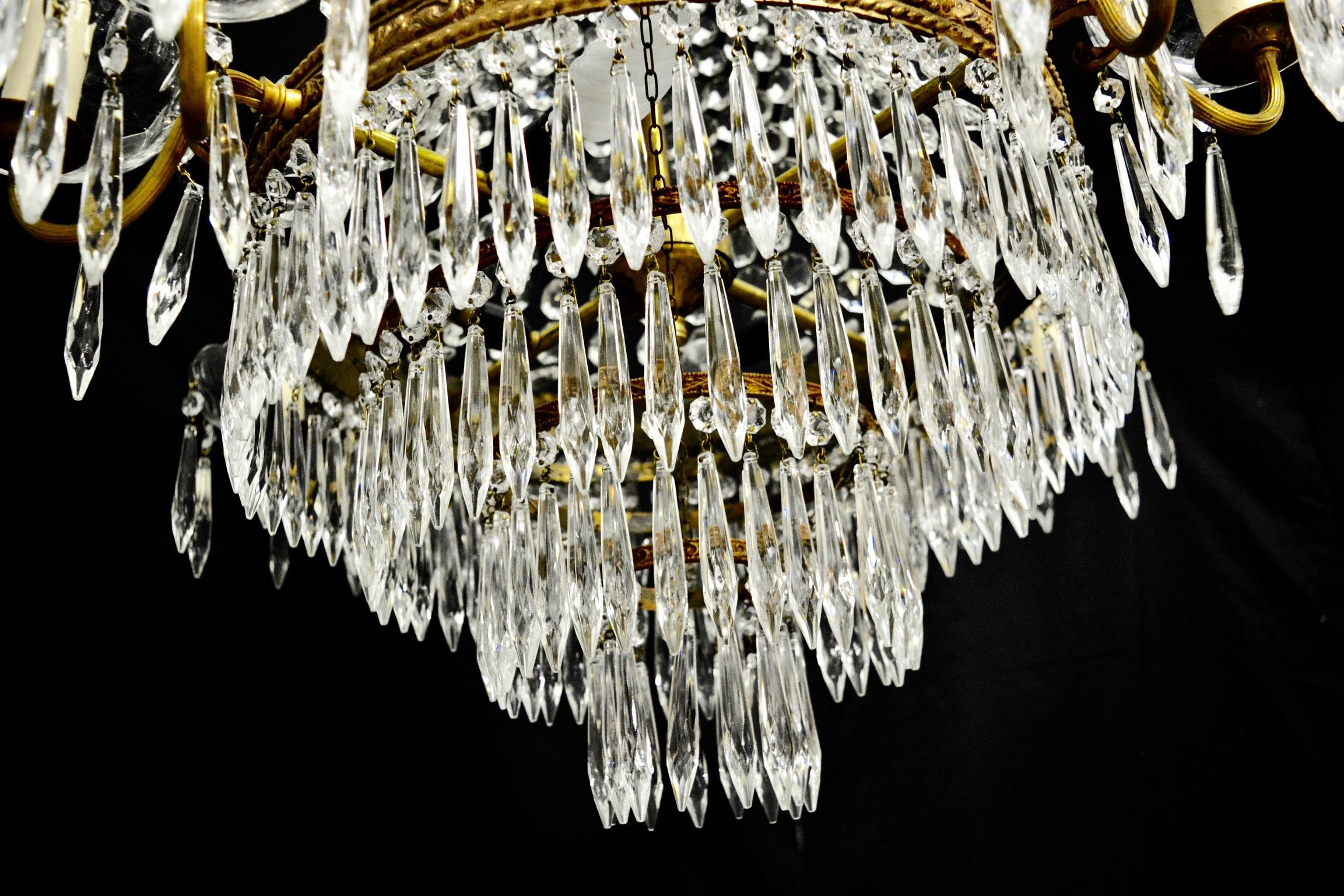 This brass Italian Empire chandelier has 12 lights. Octagonal botton chains hang from the top to the central frame part of the chandelier. A waterfall bottom is covered all around by icicle cut crystal drops. Glass cups holding icicle drops are
