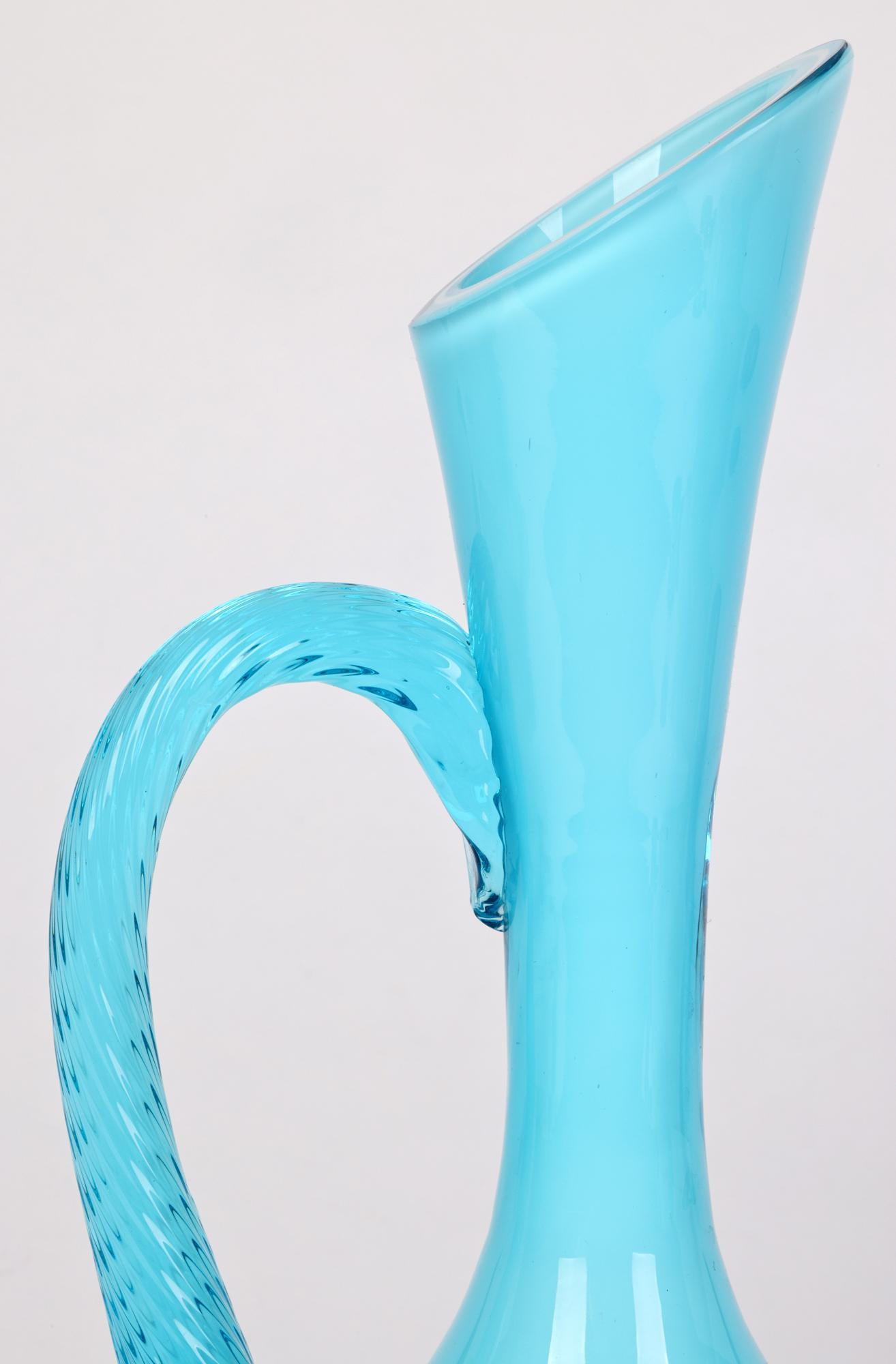 A stylish Italian mid-century turquoise cased art glass jug by Empoli. The jug stands on a flat round base with a rounded bulbous lower body and long slender neck widening towards the top. The top has been slice cut at an angle to form the pouring