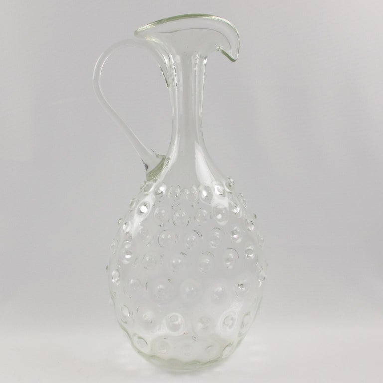 Elegant 1950s, tall pitcher, decanter manufactured by Empoli, Italy. Beautiful highly decorative Etruscan shape with hobnail pattern. Hand-blown glass in Murano, Italy.
Measurements: 7.87 in. wide (20 cm) x 5.12 in. deep (13 cm) x 15.37 in. high