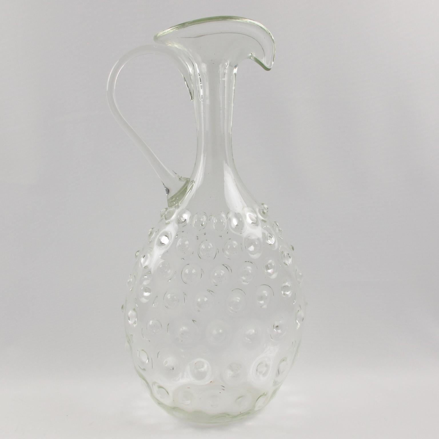 This stunning Empoli, Italy, hand-blown art glass pitcher or decanter is a gorgeous piece of Italian craftsmanship. This tall pitcher features an Etruscan shape with a hobnail pattern and was hand-crafted in Murano, Italy, circa 1950. It is the