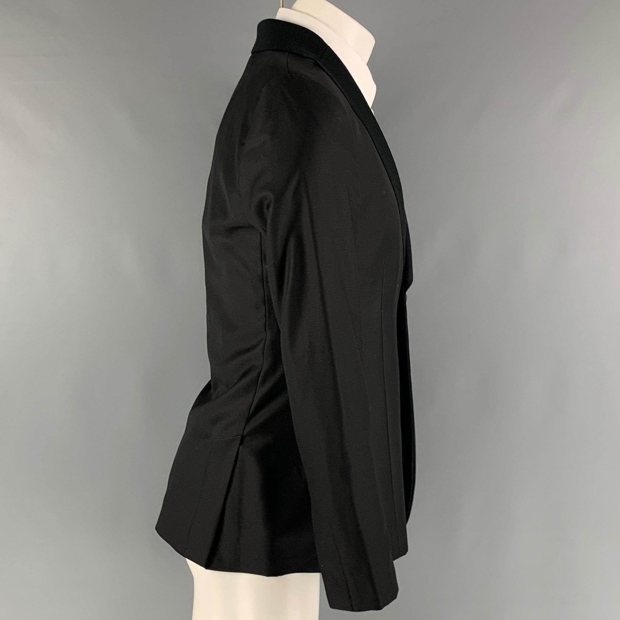 Le manteau sport 'MILANO' d'EMPORIO ARMANI est réalisé dans un tissu noir de laine et de soie avec une doublure complète. Il présente un revers à cran, des poches latérales et se ferme par un seul bouton. Fabriquées en Italie. Excellent état