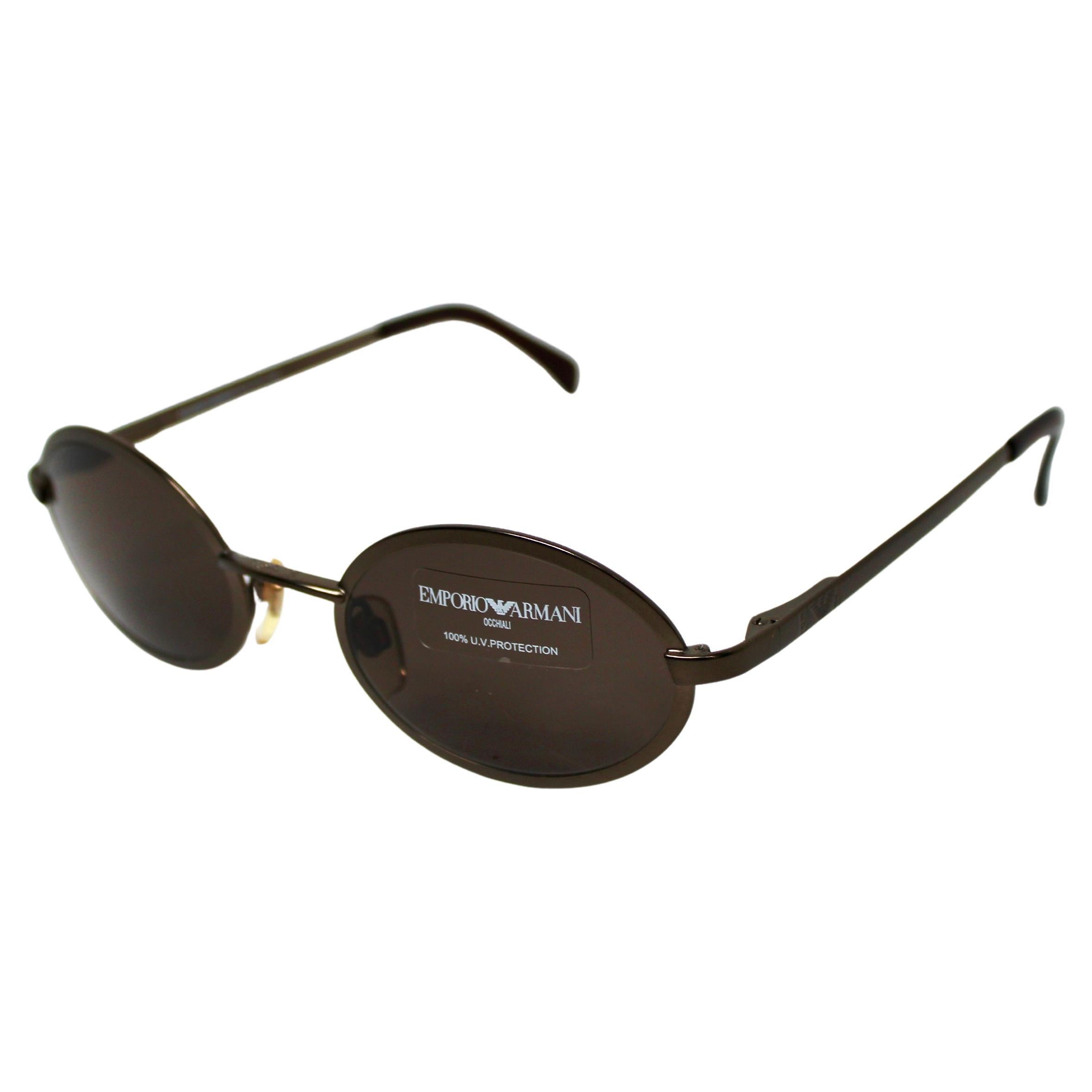 Las gafas de sol con montura metálica ovalada Emporio Armani de alrededor de los años 90 encarnan la sofisticación atemporal y el estilo elegante y vintage. Fabricadas con una resistente montura metálica en tono bronce, estas gafas de sol presentan