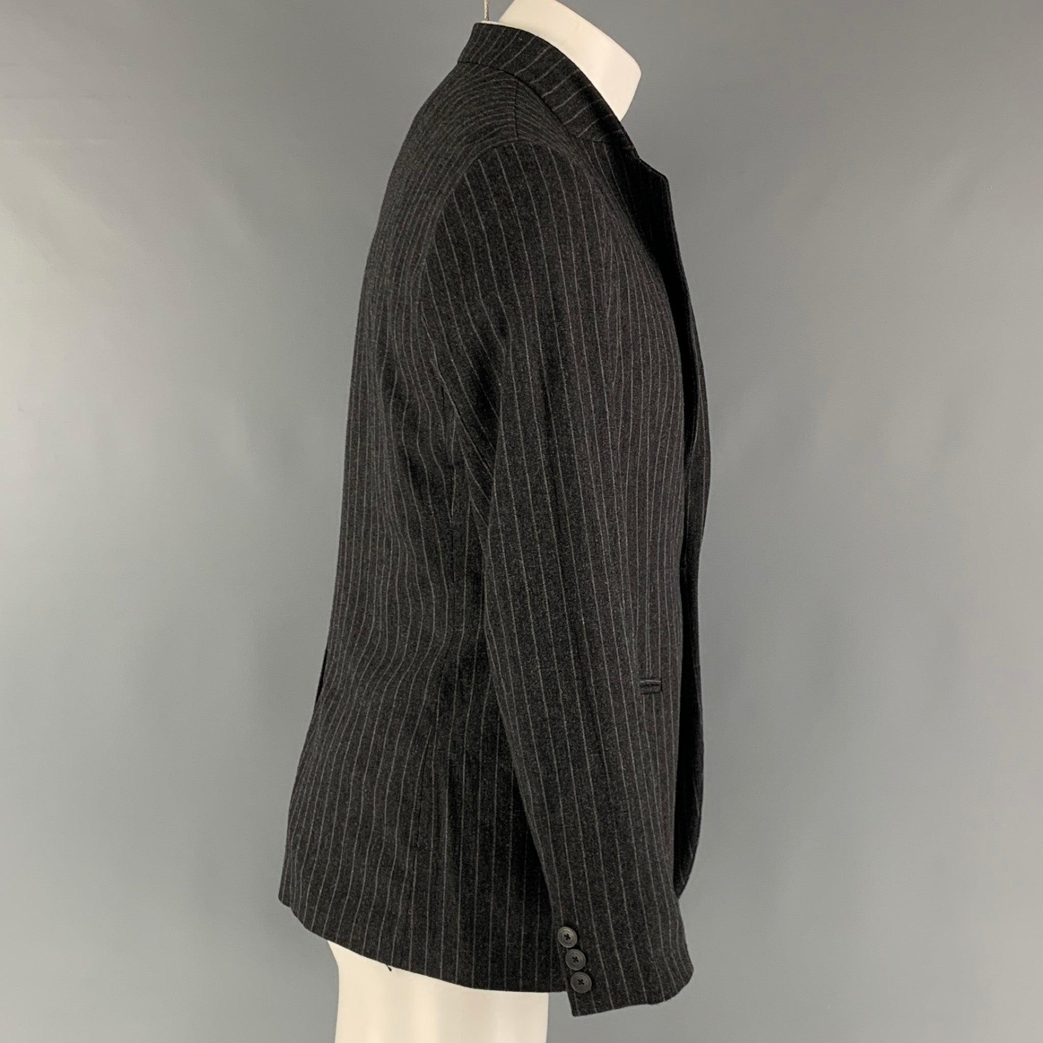 Le manteau sport 'Johnny Line' d'EMPORIO ARMANI se compose d'une doublure intégrale en laine rayée gris et anthracite, d'un col montant, de poches passepoilées, d'une seule fente au dos et d'une fermeture à bouton unique. Fabriquées en Italie.