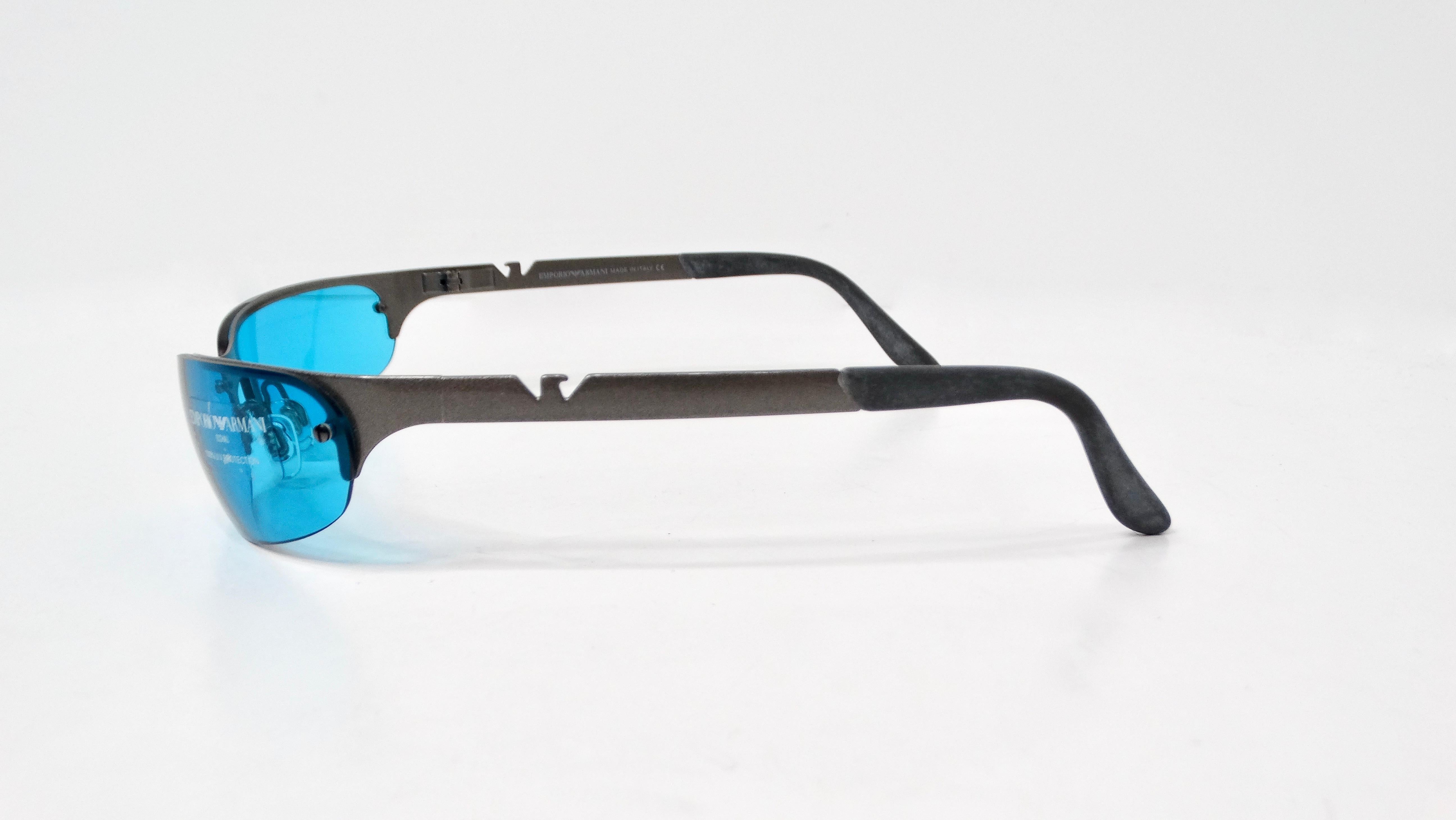 The Emporio Armani Y2K 203-S Skinny Blue Tinted Lens Metal Frame Sunglasses encapsulate the essence of early 2000s fashion with a modern twist. Designed with an thin oval shape and a distinctive shield-like style, these sunglasses boast a striking