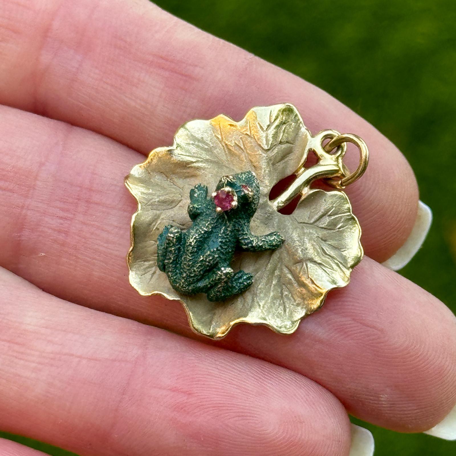 This charming and whimsical piece of jewelry features a 3-D green enamel frog with red eyes resting upon a lily pad all crafted from 14 karat yellow gold. The design captures the essense of nature with intricate detailing. This unique work of art