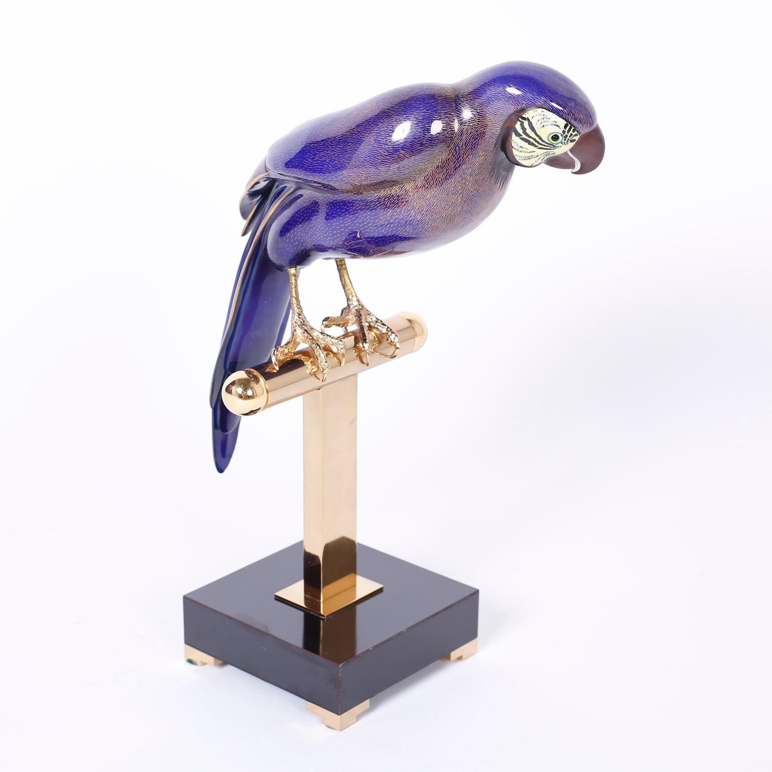 Art deco style parrot or bird decorated with an alluring indigo blue enamel over brass and perched on a polished and lacquered perch set on a streamlined base. Signed Mangani Oggetti on the inside of the tail feather.