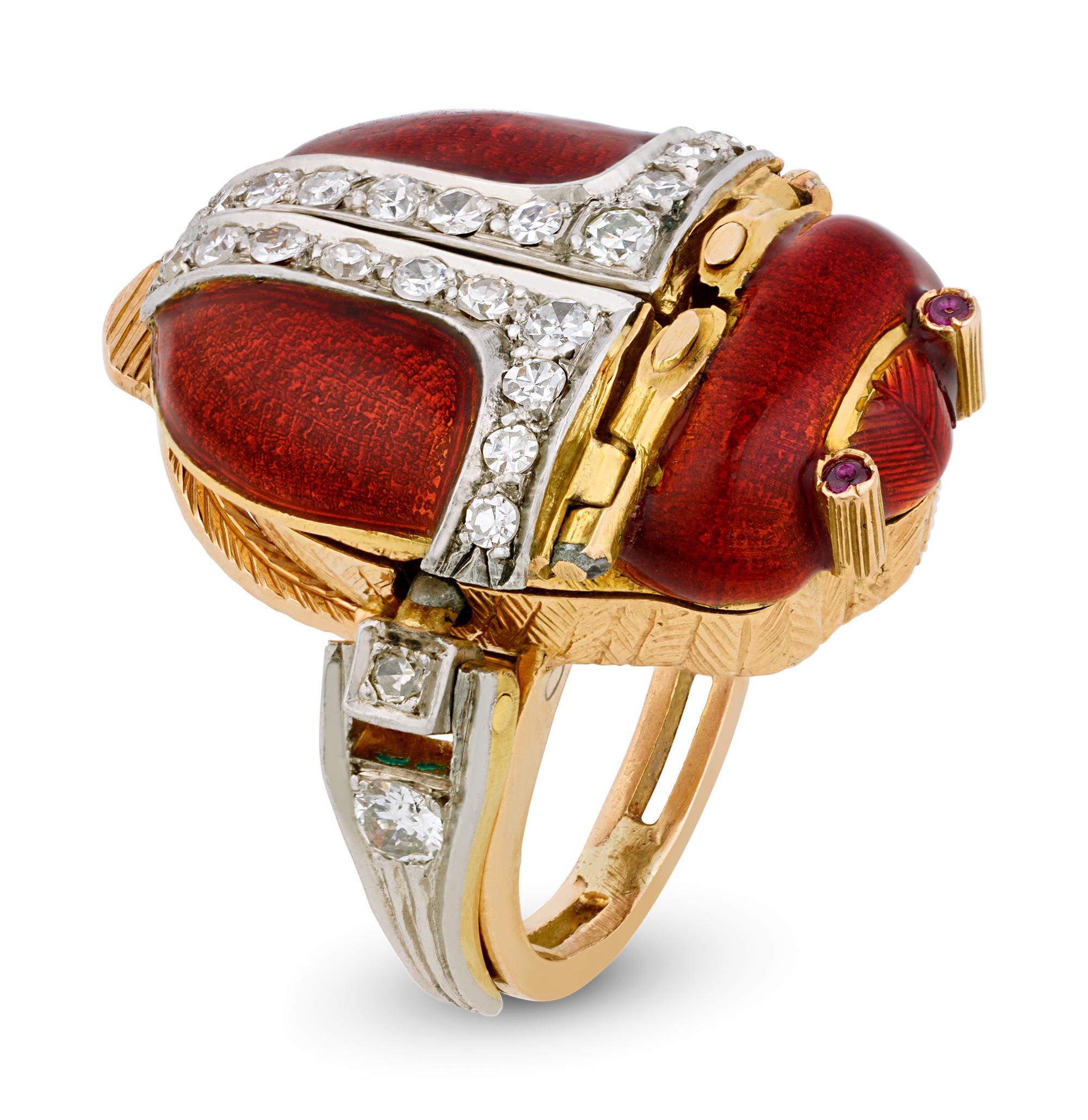 Cleverly disguised as an elegant jeweled scarab, this rare Egyptian Revival-style platinum and 18K yellow gold ring conceals a delightful secret within its artistic form. The striking rust-red enamel body is adorned with 23 high-quality single cut
