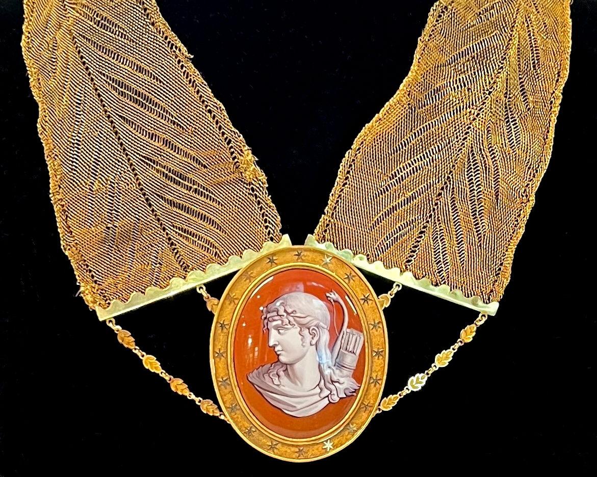 Notre collier ancien, fabriqué à partir d'une chaîne en or, comporte un pendentif avec un cadre en bronze doré représentant Artémis avec un arc sculpté et un carquois en grisaille sur un fond rouge rouille. Dans la mythologie grecque, Artémis était