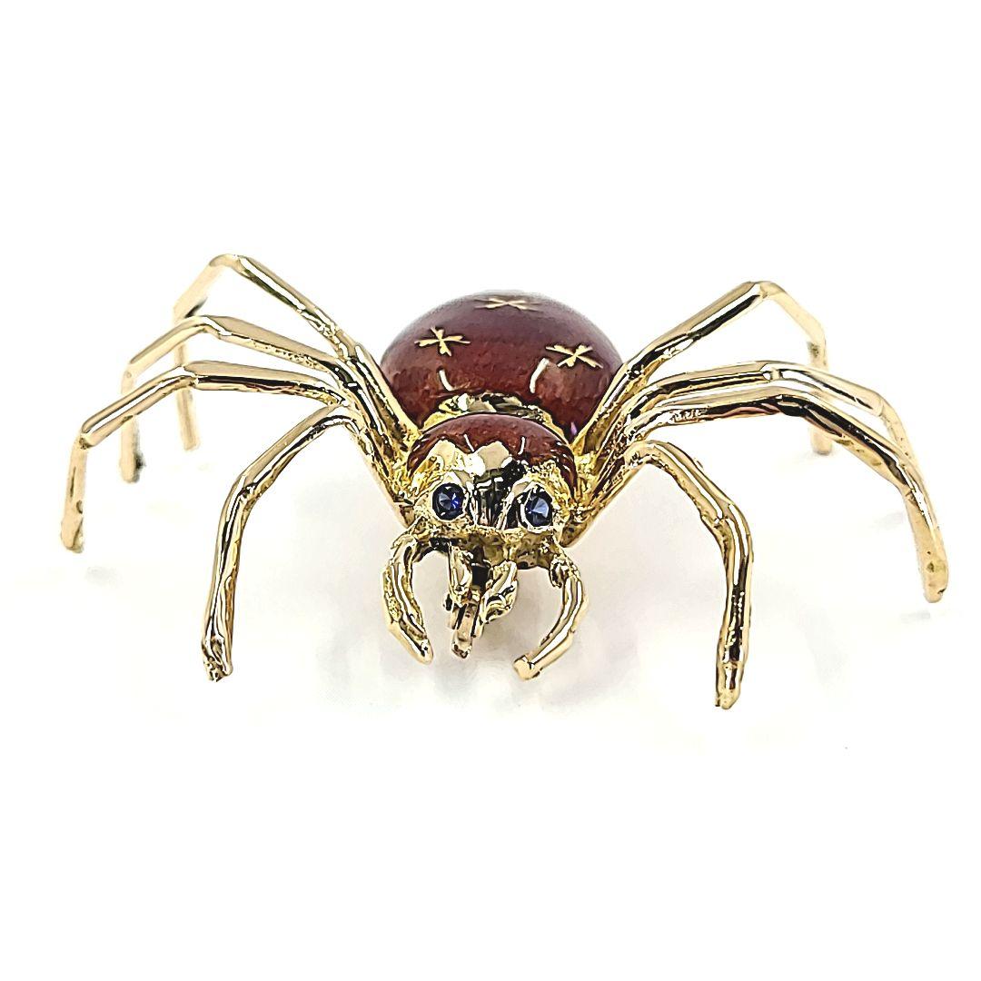 18 Karat Yellow Gold Spider Pin Featuring Reddish Brown Enamel and 2 Round Sapphire Eyes. 1.5 Inches Long by 1.75 Inches Wide. Finished Weight Is 10 Grams.