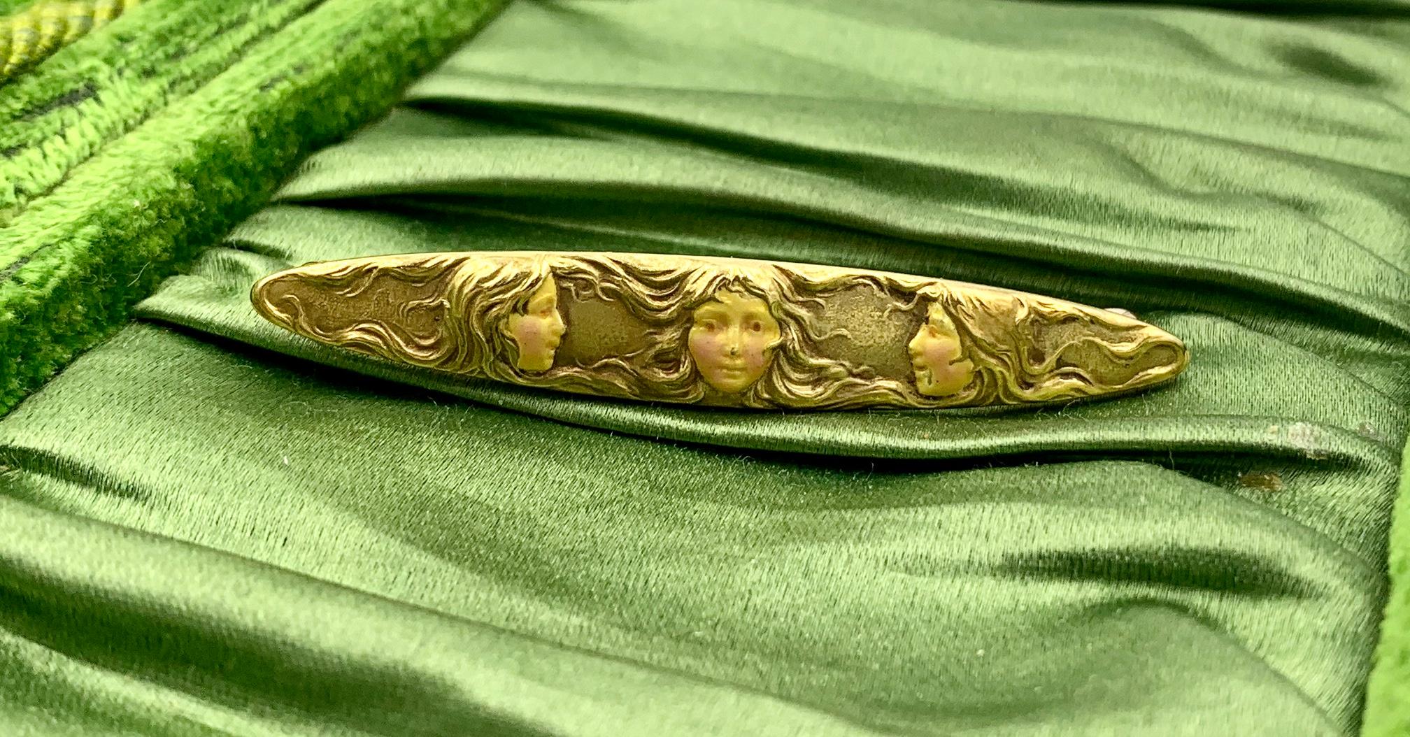 A spectacular Art Nouveau brooch with images of three maidens in 14 Karat Gold with fine Enamel decoration.  The extraordinary Art Nouveau brooch features the faces of three women.  The women's faces are decorated with enamel.  The women's hair