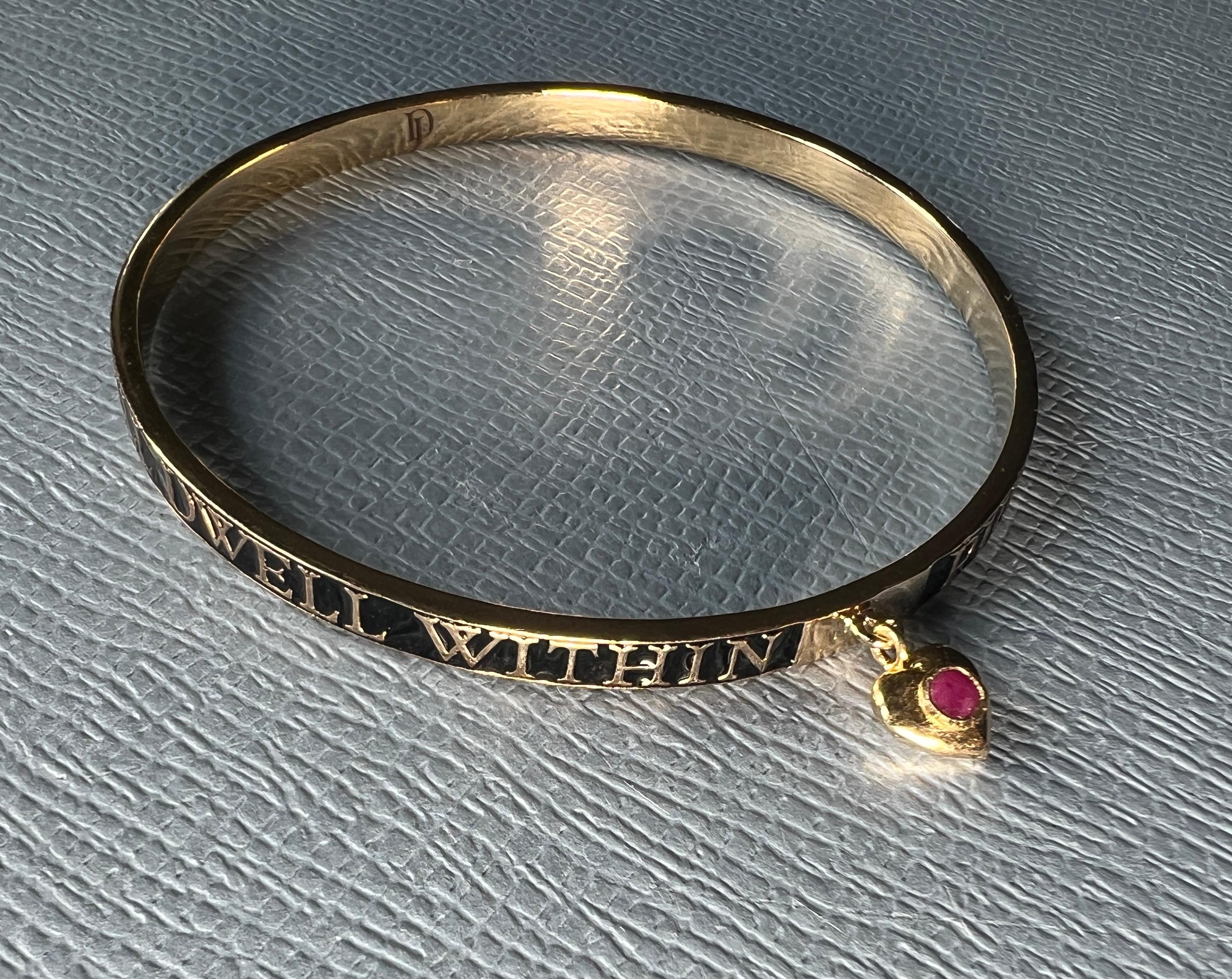 Pulsera de esmalte negro Corazón de rubí 

Placa de oro de 14 quilates con esmalte negro pintado a mano y un corazón colgante engastado con un rubí.

El texto de la pulsera dice Purifica tu corazón y la luz infinita habitará en tu