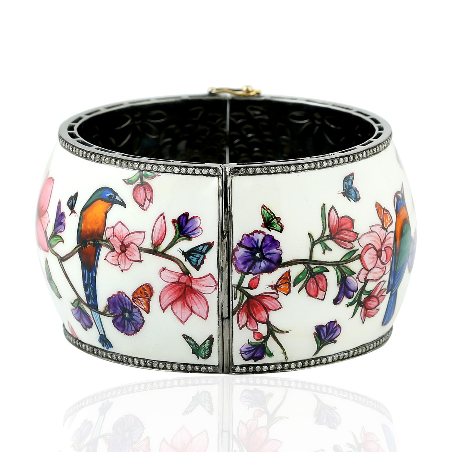 This cuff bracelet features a stunning bird design that has been carefully enameled to showcase its intricate details and colors. The edges of the cuff are decorated with a breathtaking pave of diamonds that catch the light and add a touch of