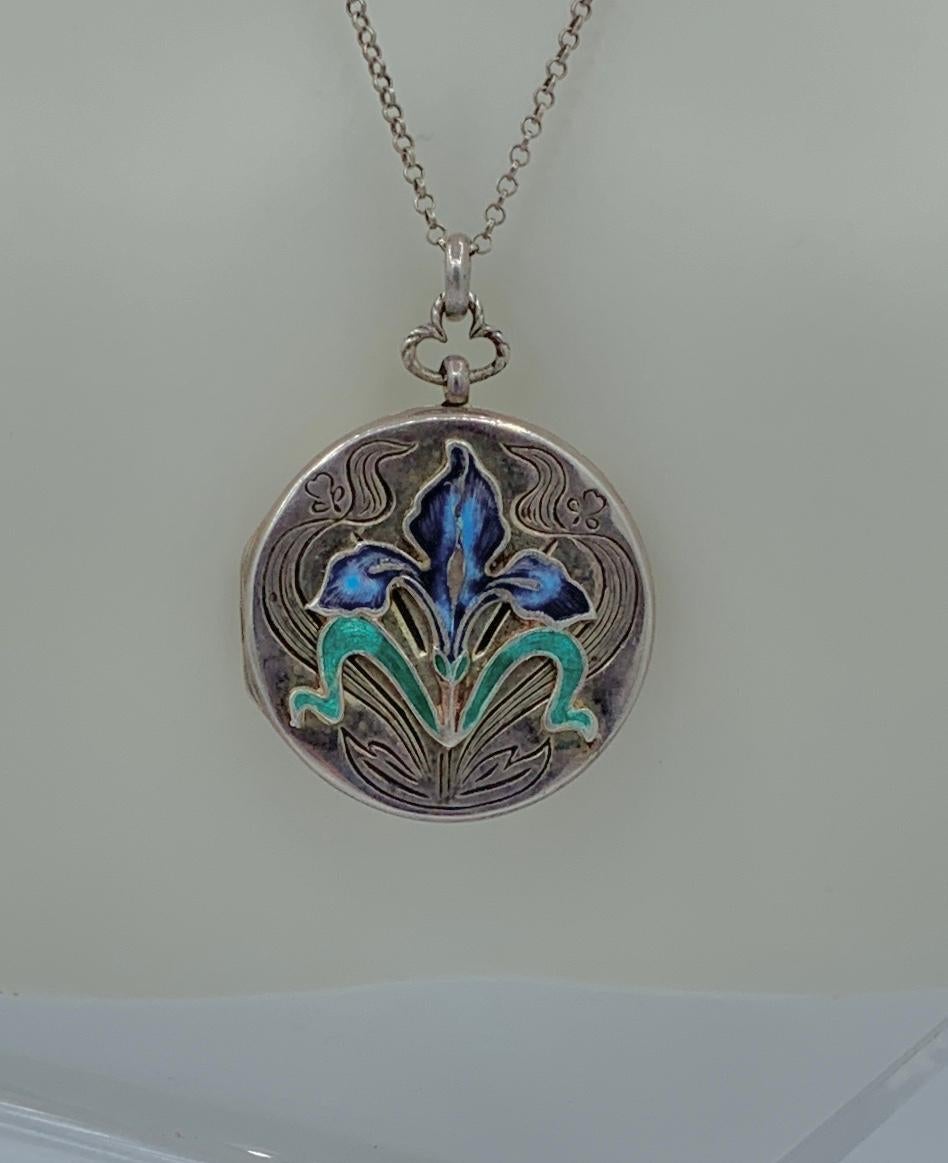 THIS IS A GORGEOUS AND RARE ART NOUVEAU LOCKET NECKLACE WITH A STUNNING ENAMEL PURPLE IRIS FLOWER IN STERLING SILVER WITH A BEAUTIFUL RAISED DESIGN OF AN IRIS FLOWER, LEAF AND BUD MOTIF WITH FURTHER ENGRAVED ADORNMENT.
This is a stunning Sterling