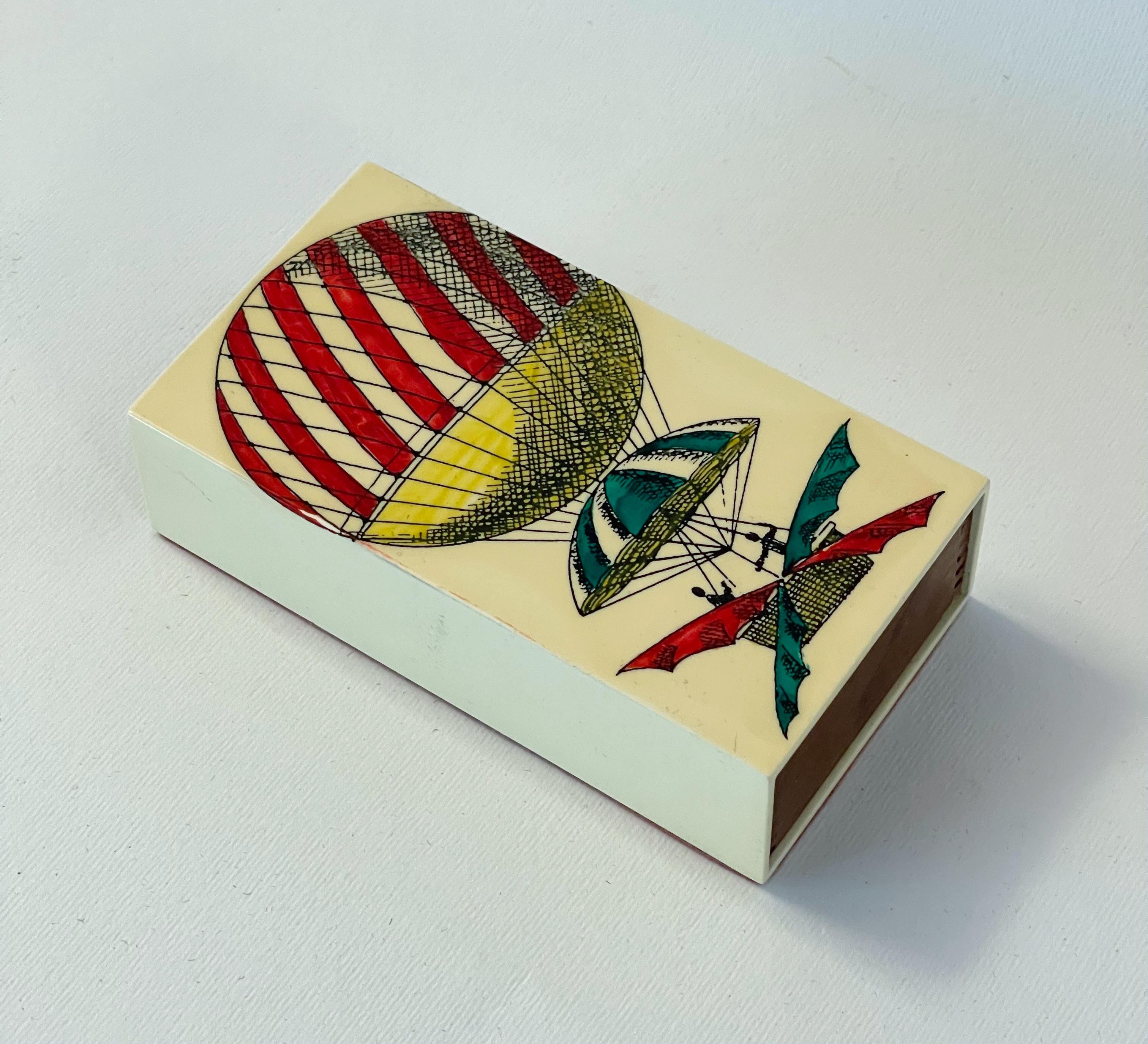 Caja de cerillas decorativa vintage con esmalte metálico que representa un globo aerostático e inserto de madera de caoba / diseñada por Piero Fornasetti, fabricada en Italia en la década de 1960
Largo: 4,5 pulgadas / Ancho: 2,5 pulgadas / Alto: 1,5
