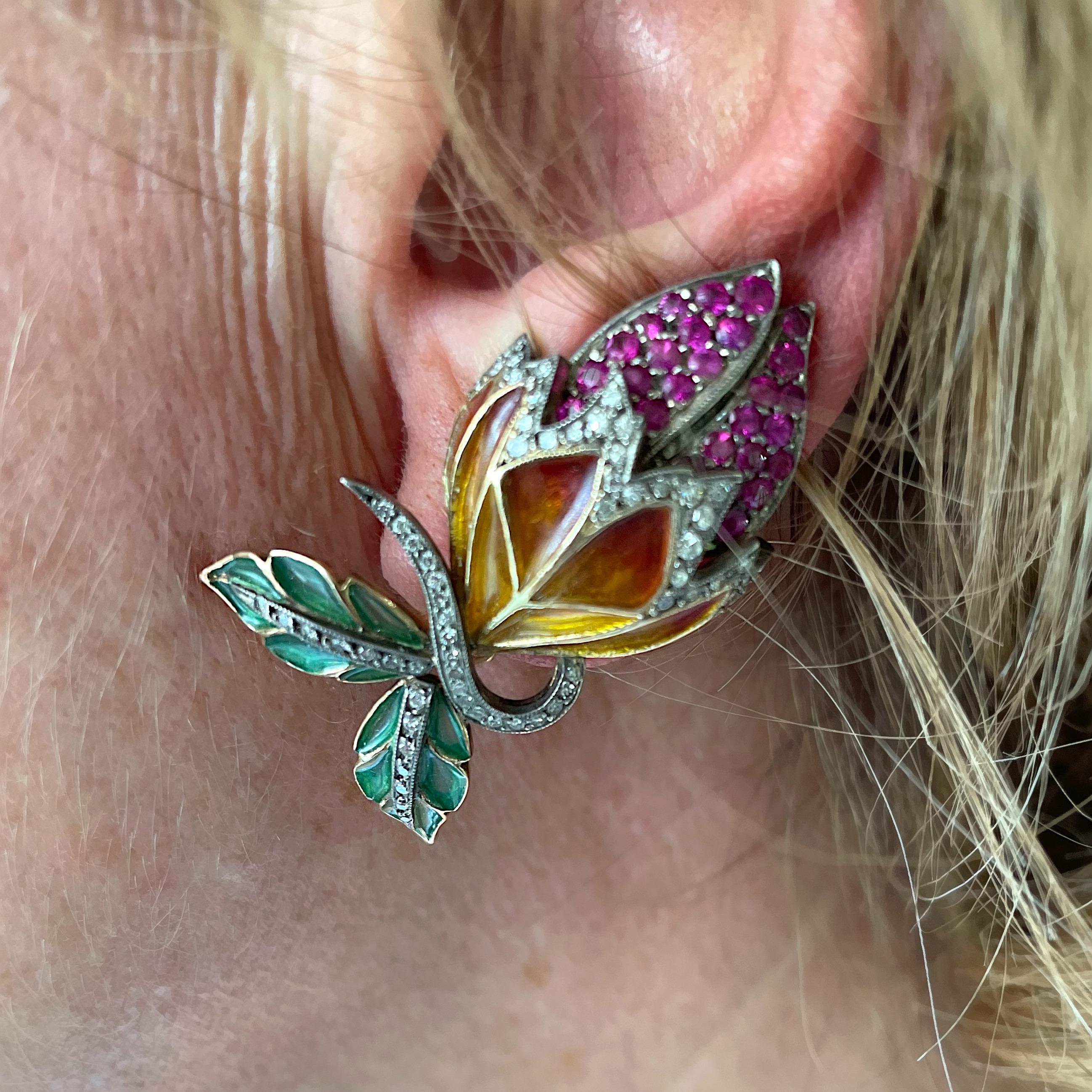 A pair of Moira bud earrings, with orange and yellow plique à jour enamel sepals and green leaves, with pavé set rubies and diamonds, mounted in gold, with silver settings. Numbered.

Moira’s eponymous collection was inspired by clients searching