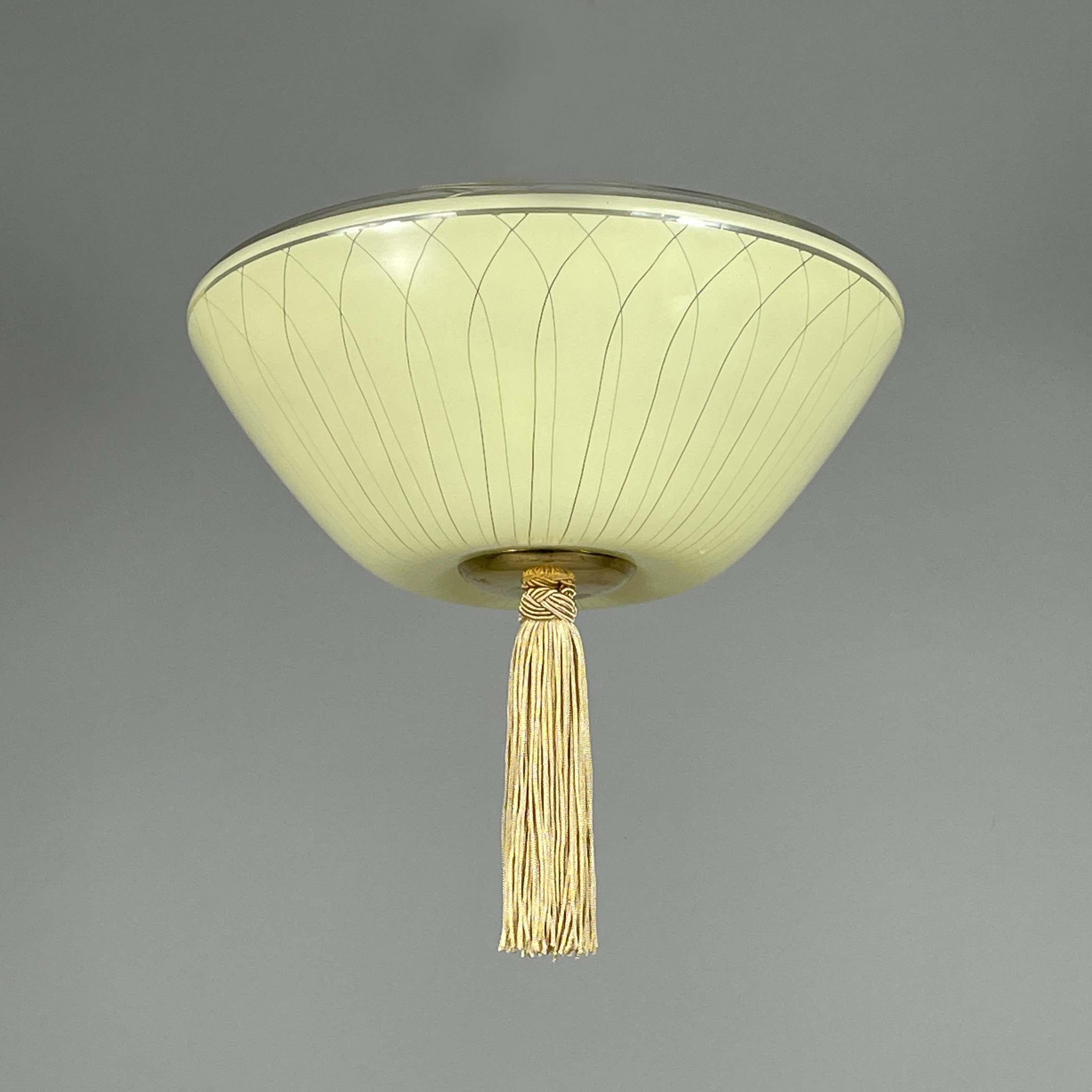 This minimalist flush mount was manufactured in the 1950s. 

The light features a distinctive mid-century Swedish design, characterized by an inverted bowl-shaped glass shade with delicate linear detailing. The shade has a pale yellow hue,